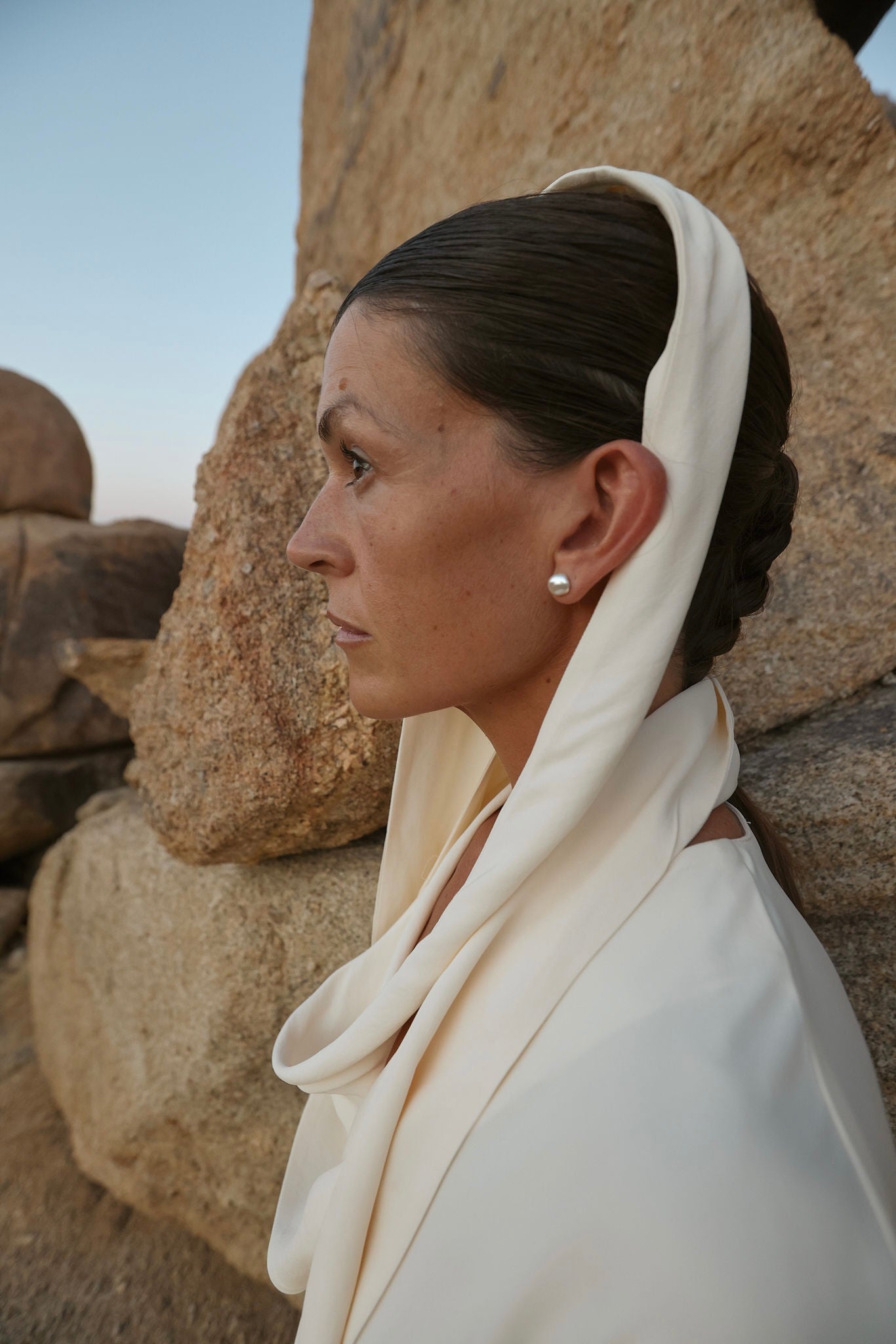 Woman wearing white keshi pearls and dress against a rocky background