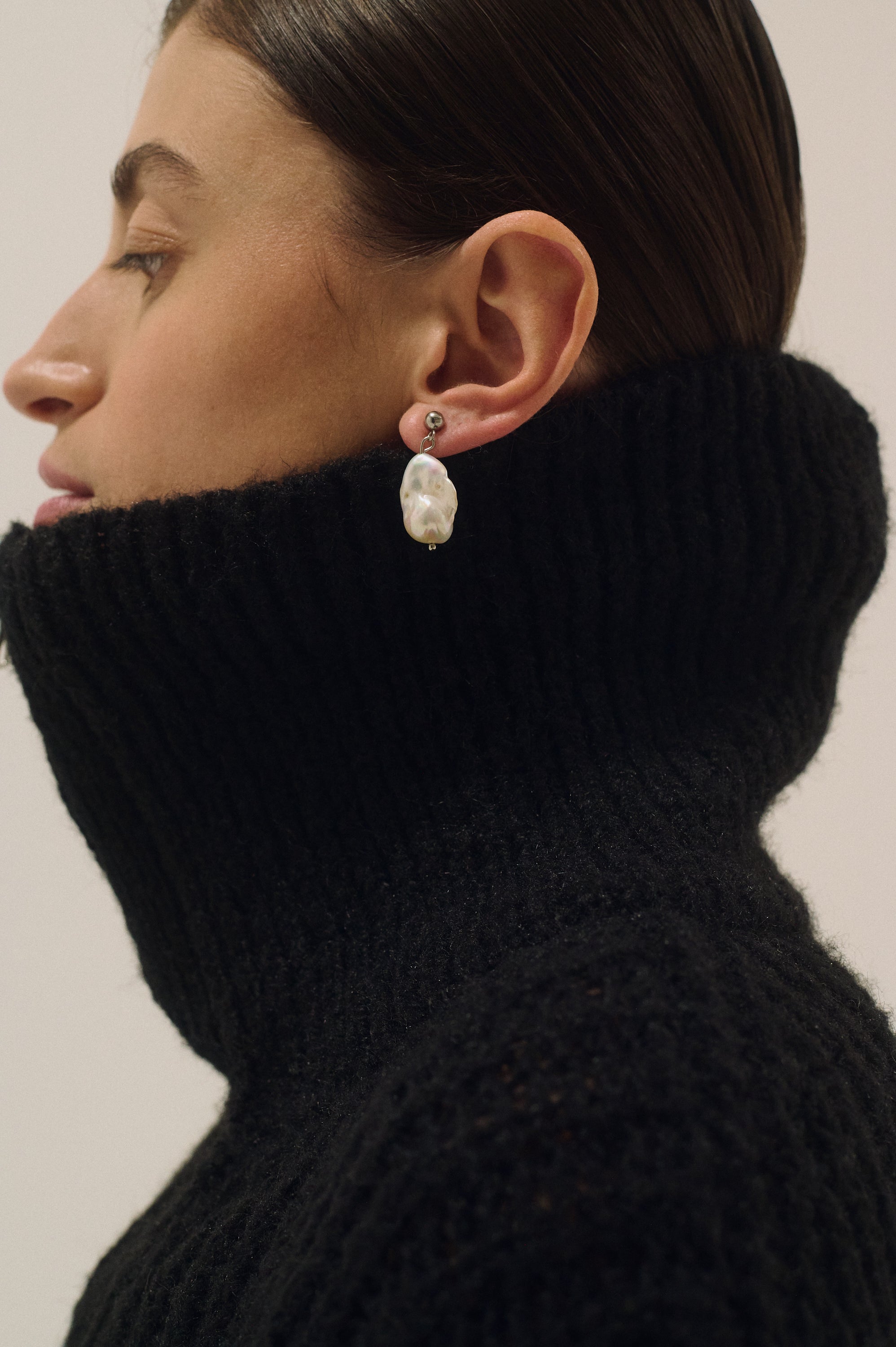 Person wearing a black turtleneck and pearl earrings against a neutral background
