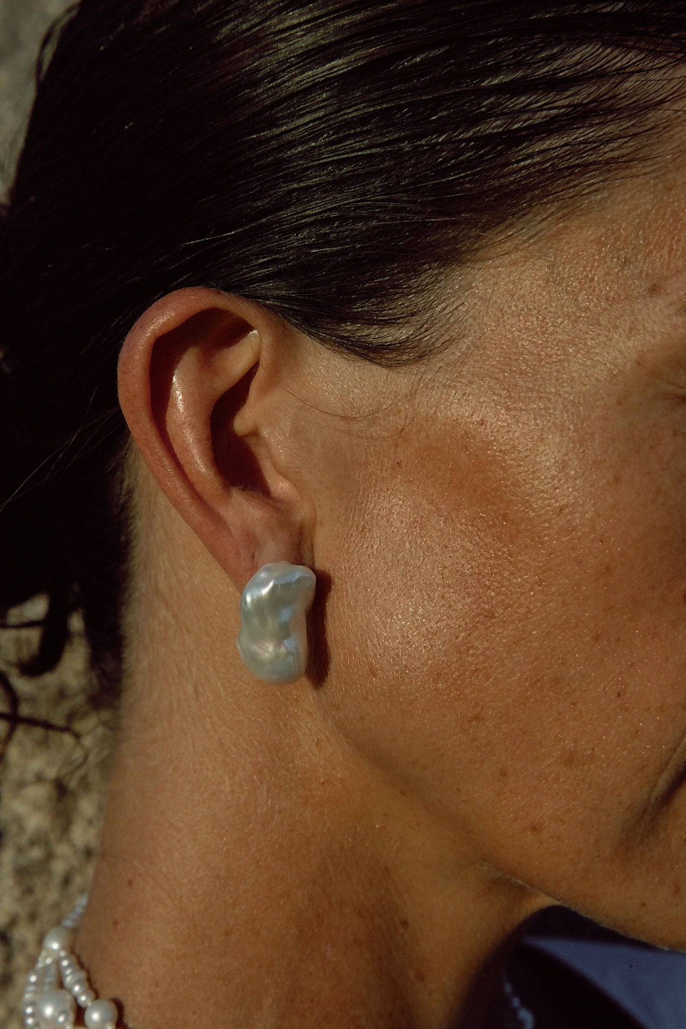 Close-up of handmade baroque pearl stud earrings on model outdoors