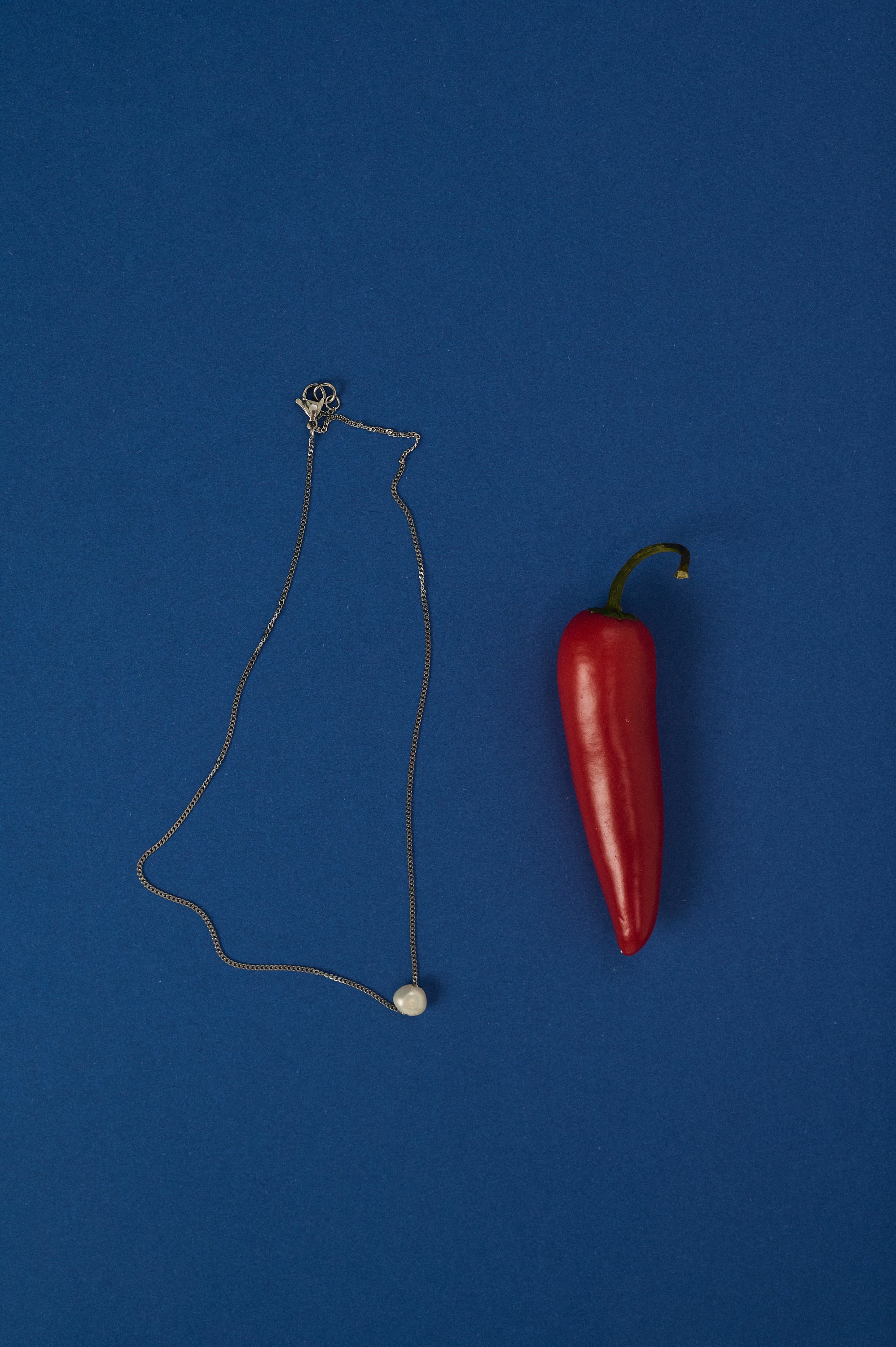 Delicate chain necklace with a single freshwater pearl pendant on blue background – minimalist jewelry design.