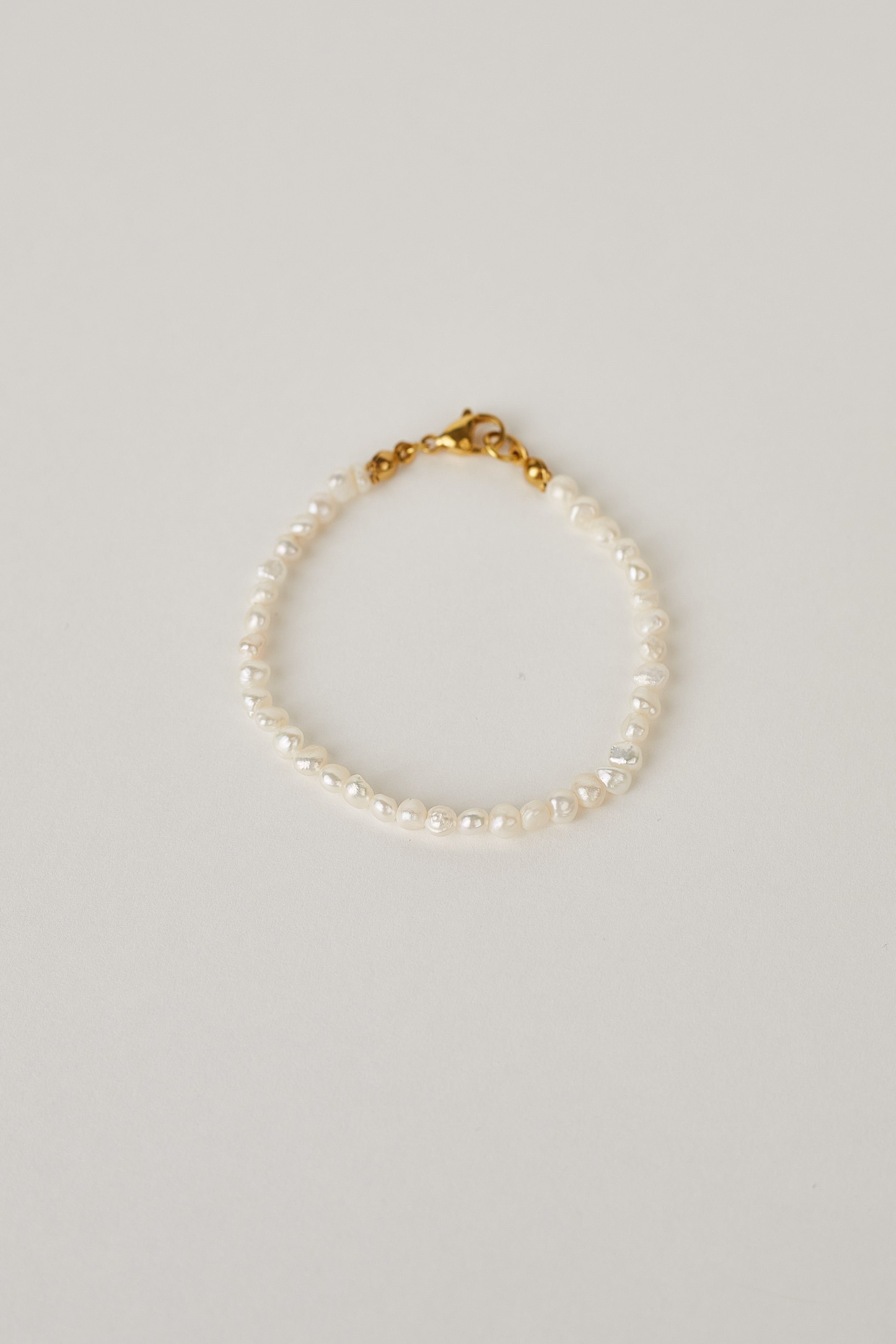 Pearl bracelet with a gold clasp on a light gray background