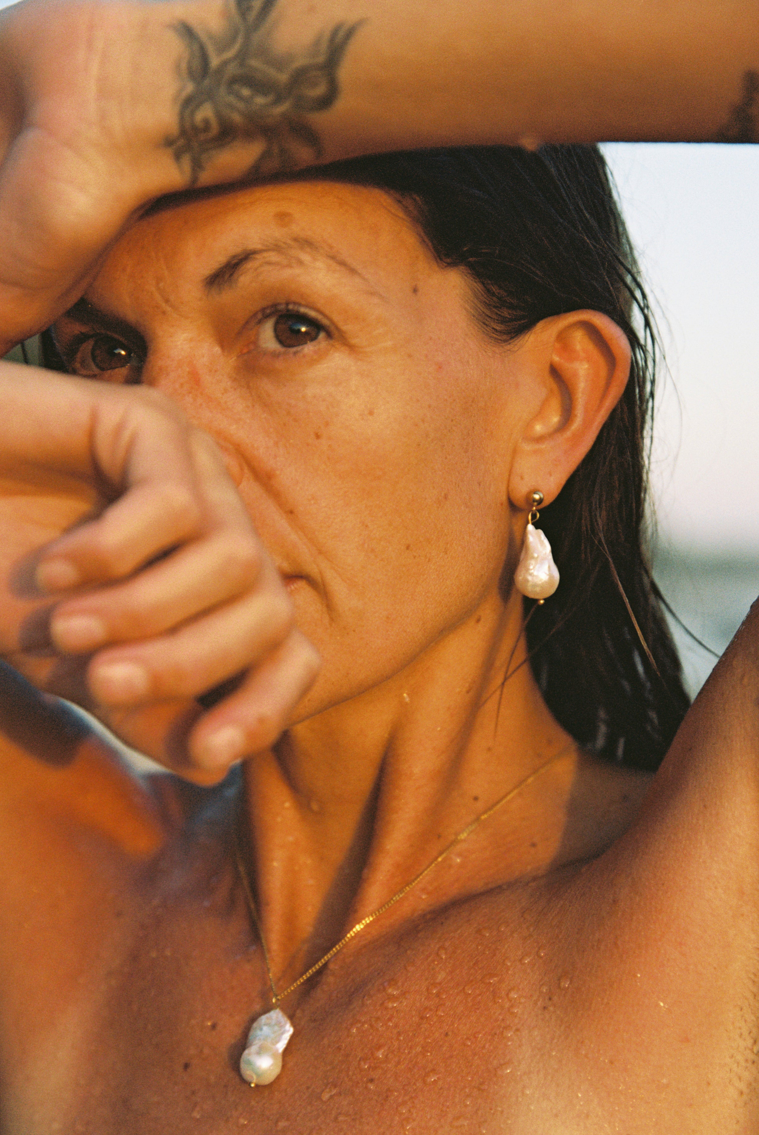 Woman wearing fine long gold chain with baroque pearl pendant and matching earrings.
