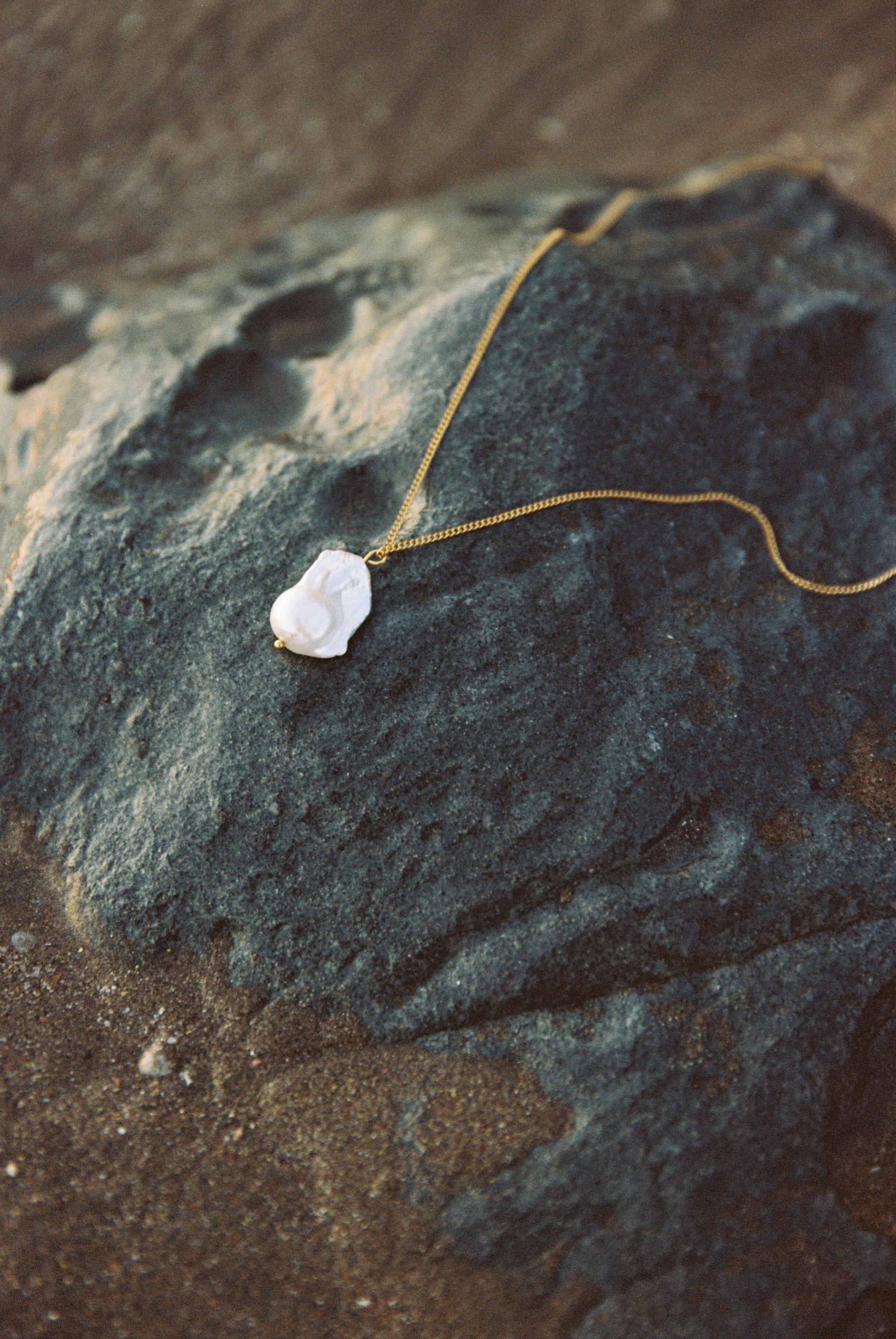 Fine gold chain with natural baroque pearl pendant on a rock, product photo.