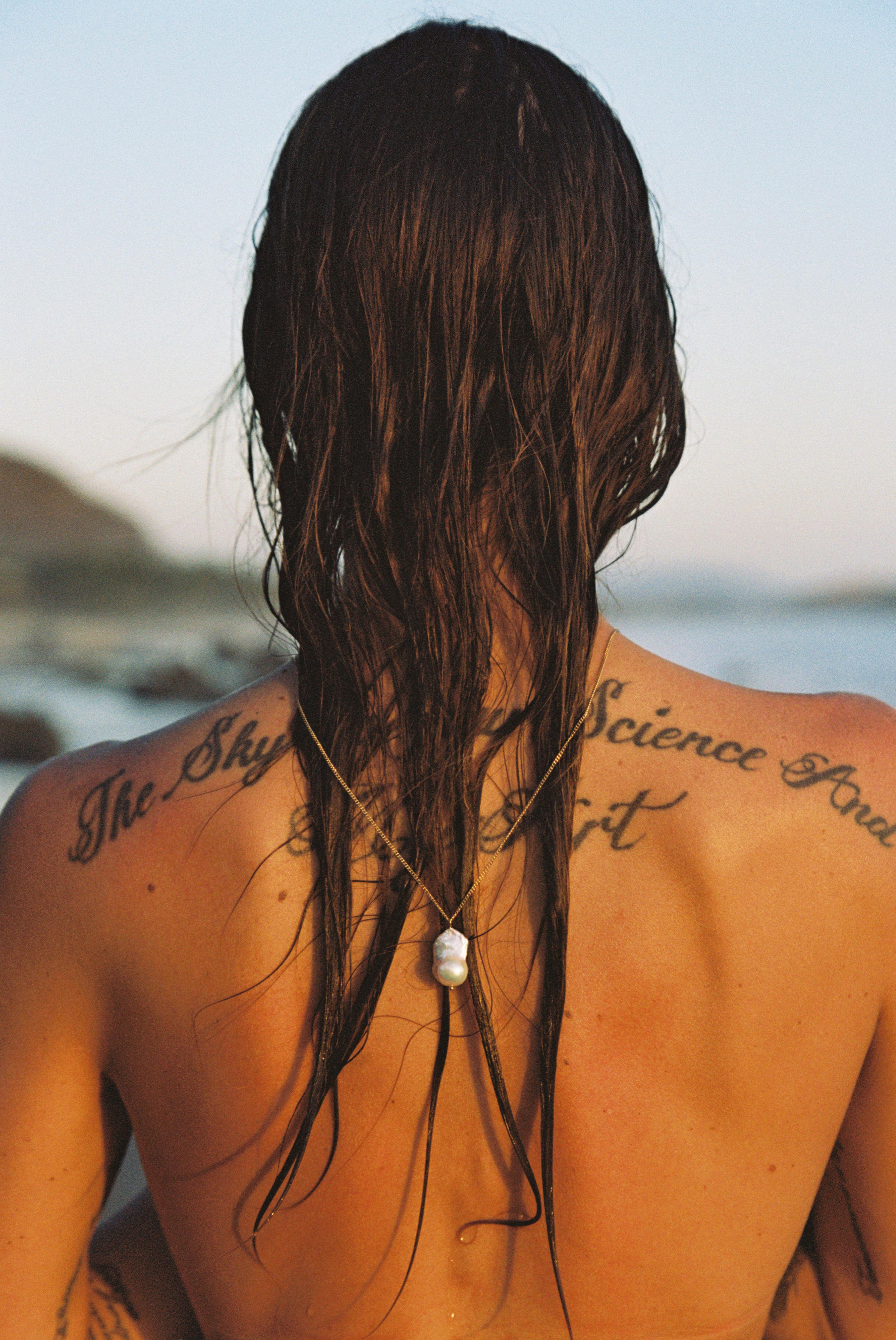 Model at the beach wearing long gold chain necklace with baroque pearl pendant.