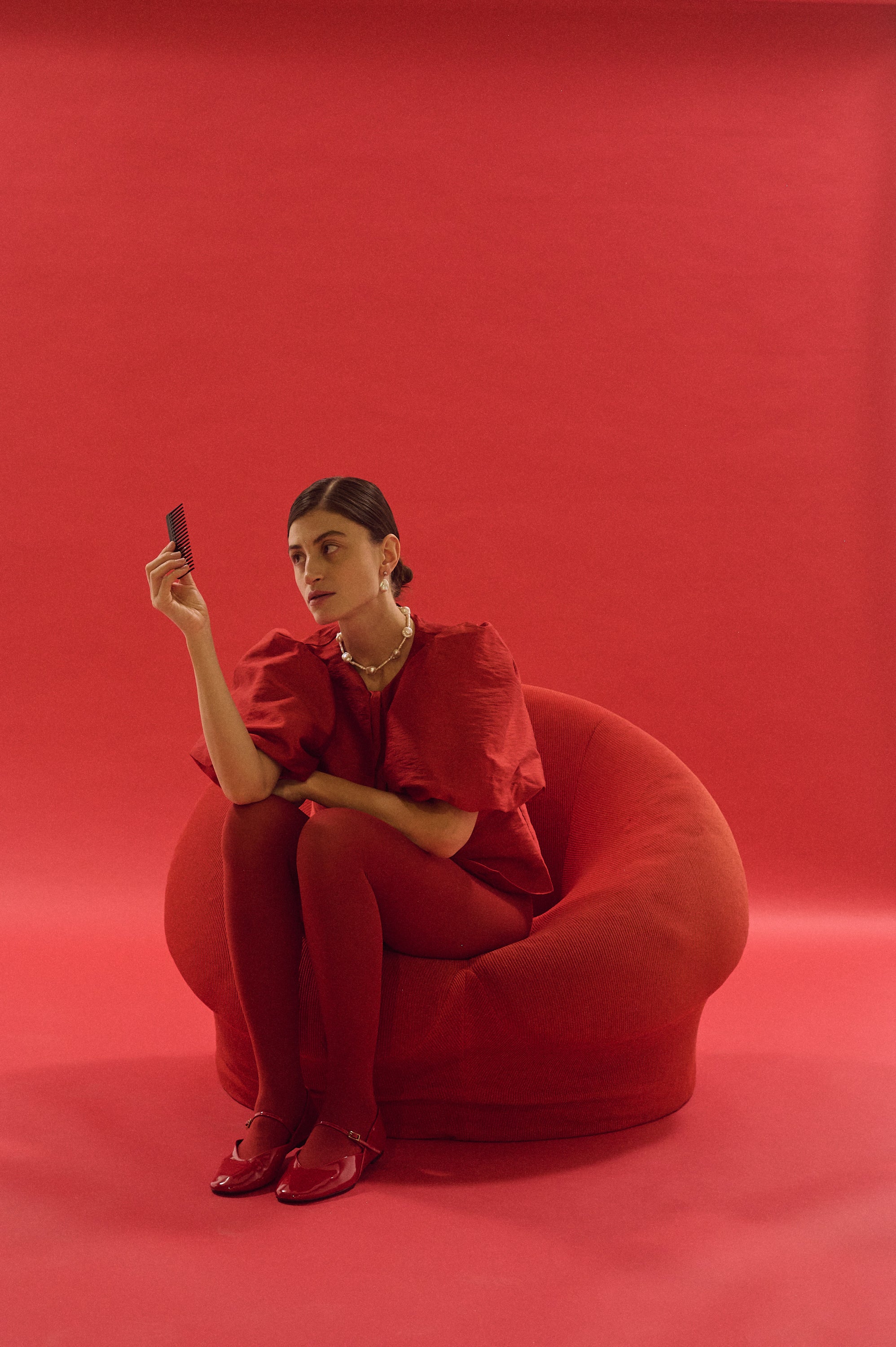 Woman seated in red chair wearing statement necklace with baroque and elongated pearls