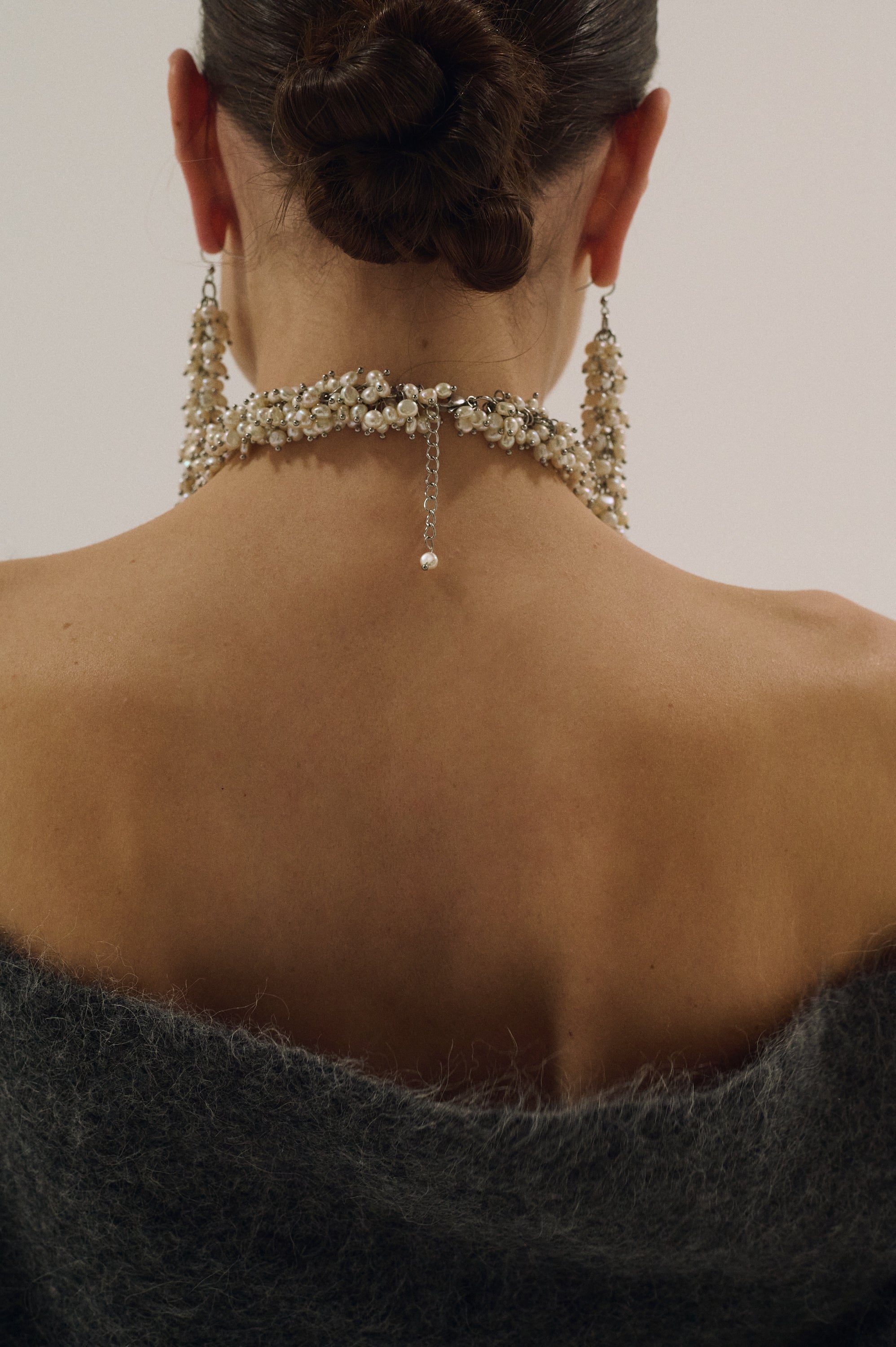 Close-up of a person wearing a delicate pearl necklace with a plain background