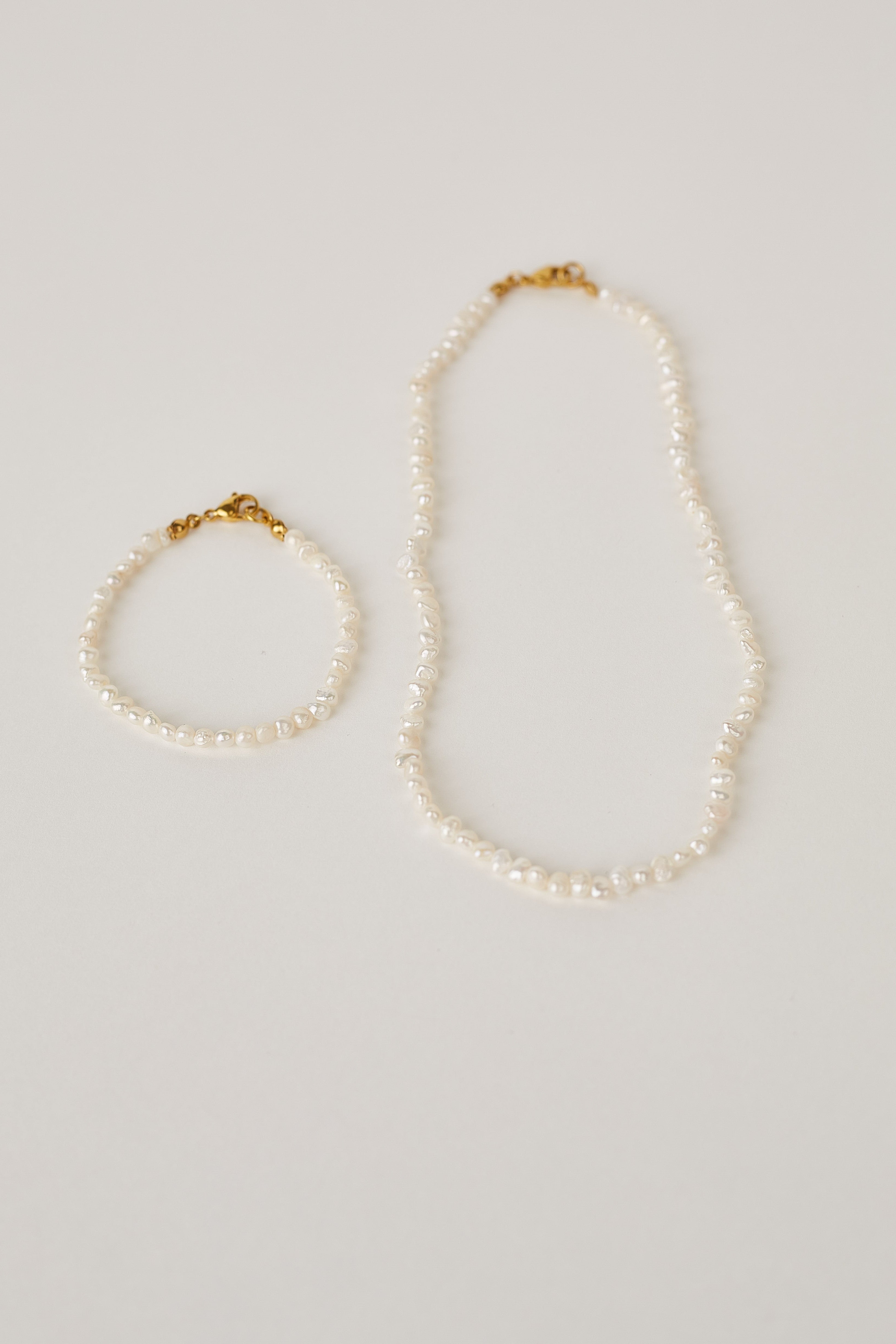 Pearl necklace and bracelet set on a light gray background