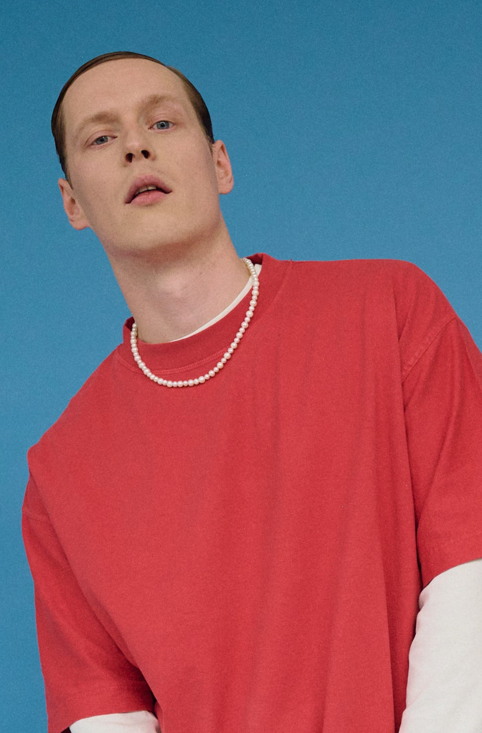 Close-up of a man in a red shirt wearing a classic round white pearl necklace.