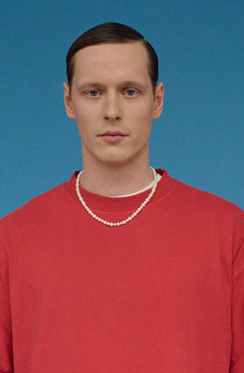 Side view of a man styling a real white pearl necklace with casual outfit.