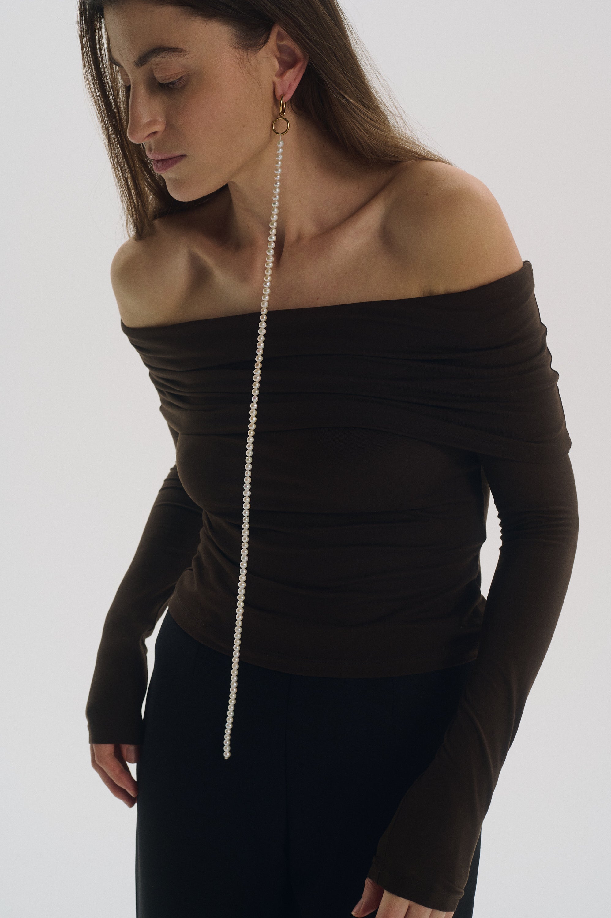 Woman wearing single long freshwater pearl earring with minimalist outfit