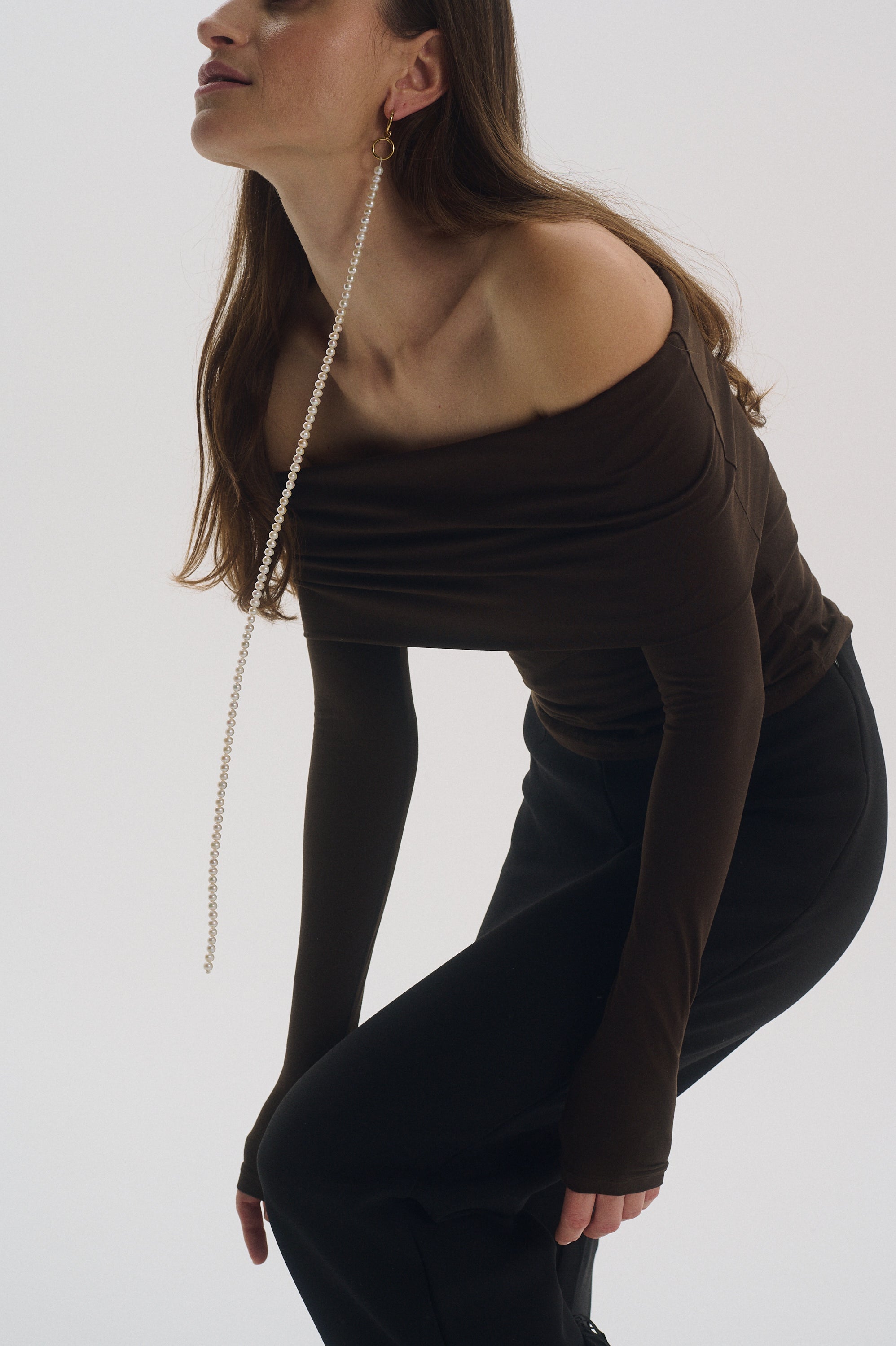 Single long drop pearl earring paired with elegant brown blouse