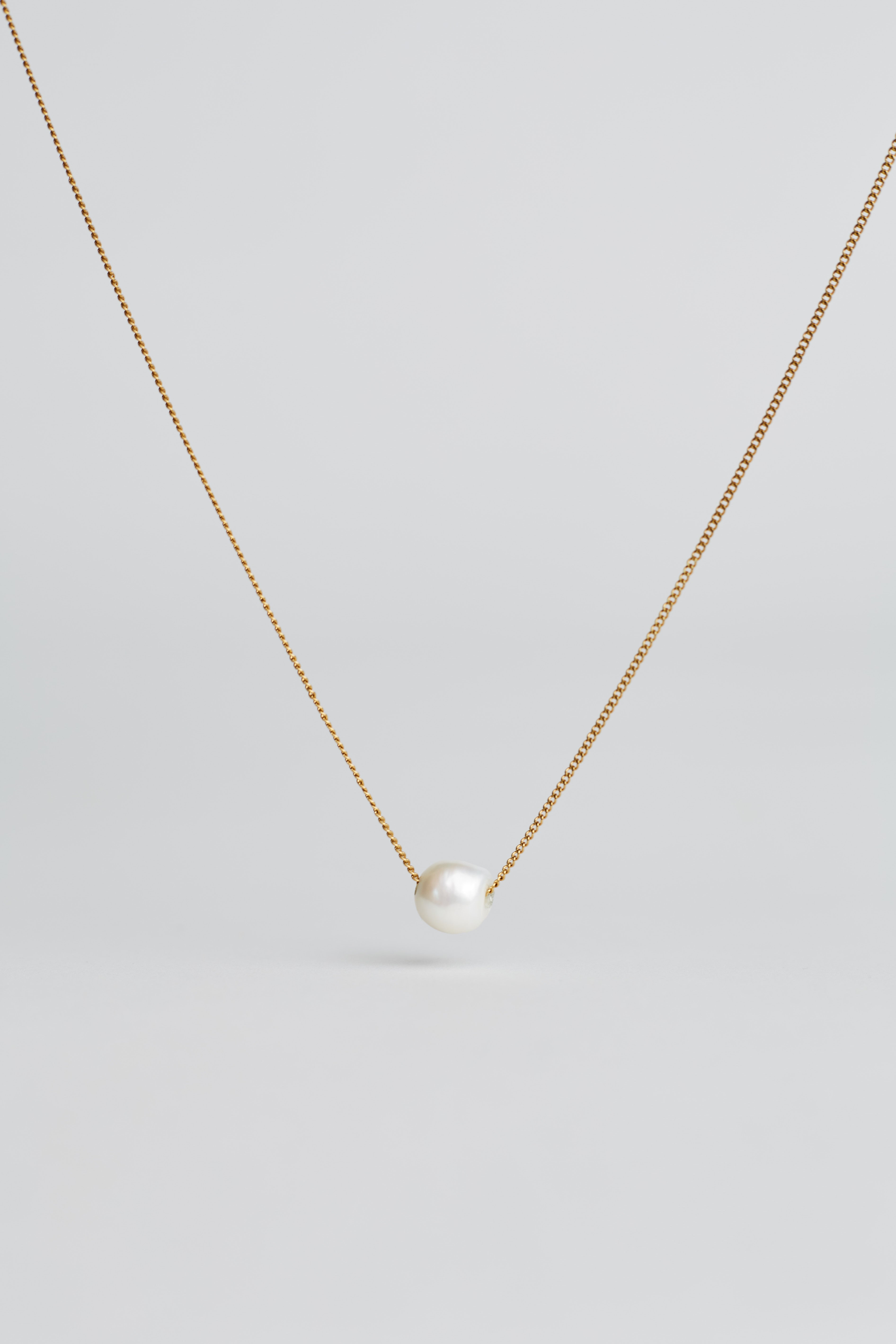 Gold necklace with a single pearl pendant on a light gray background