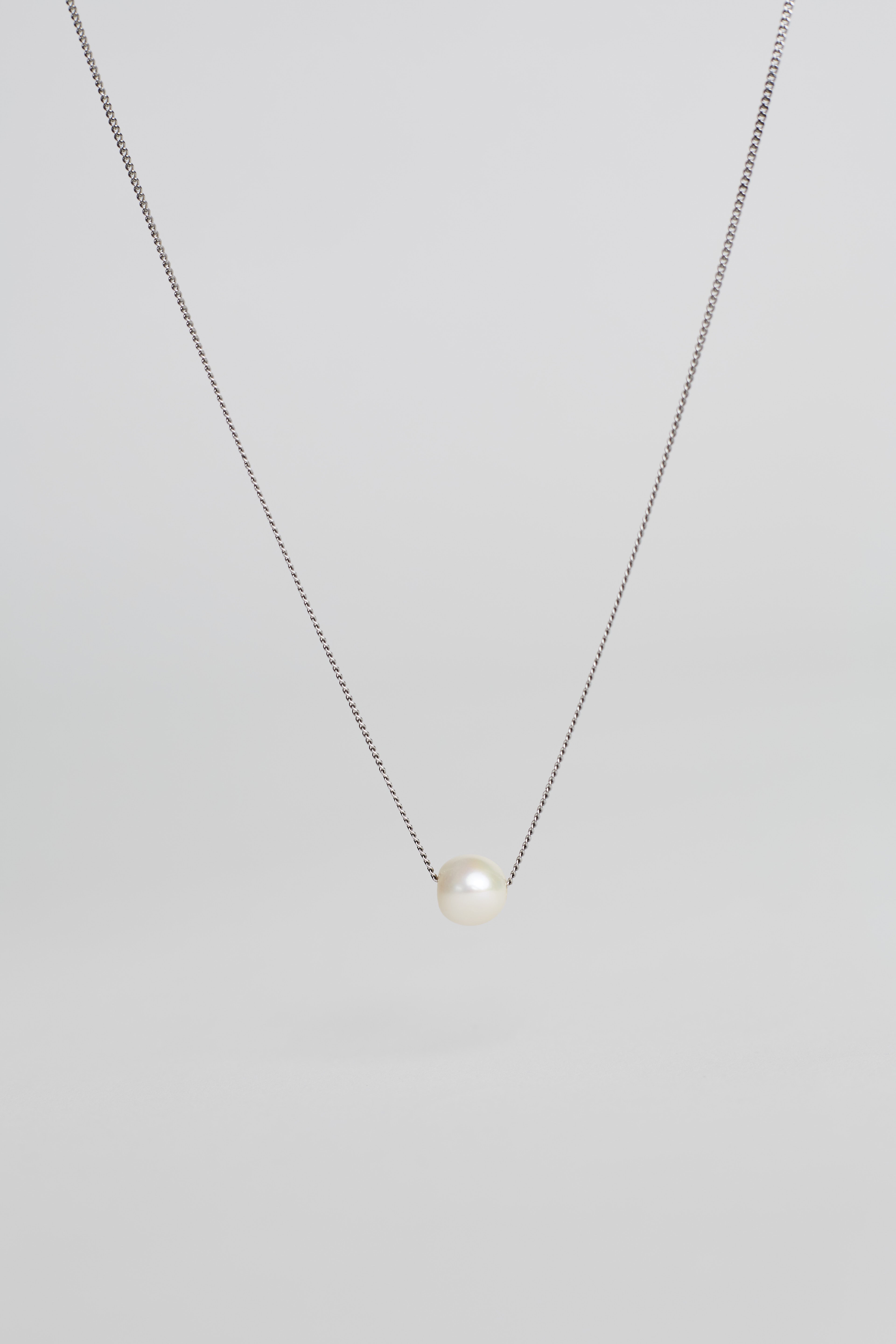 Pearl necklace on a thin chain against a light gray background