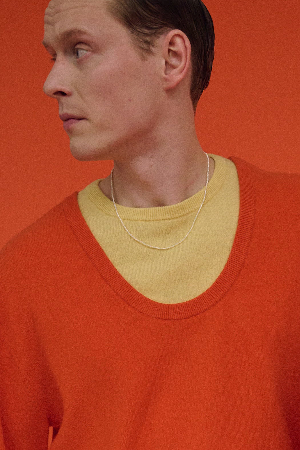 Man wearing tiny freshwater pearl necklace styled with orange sweater.