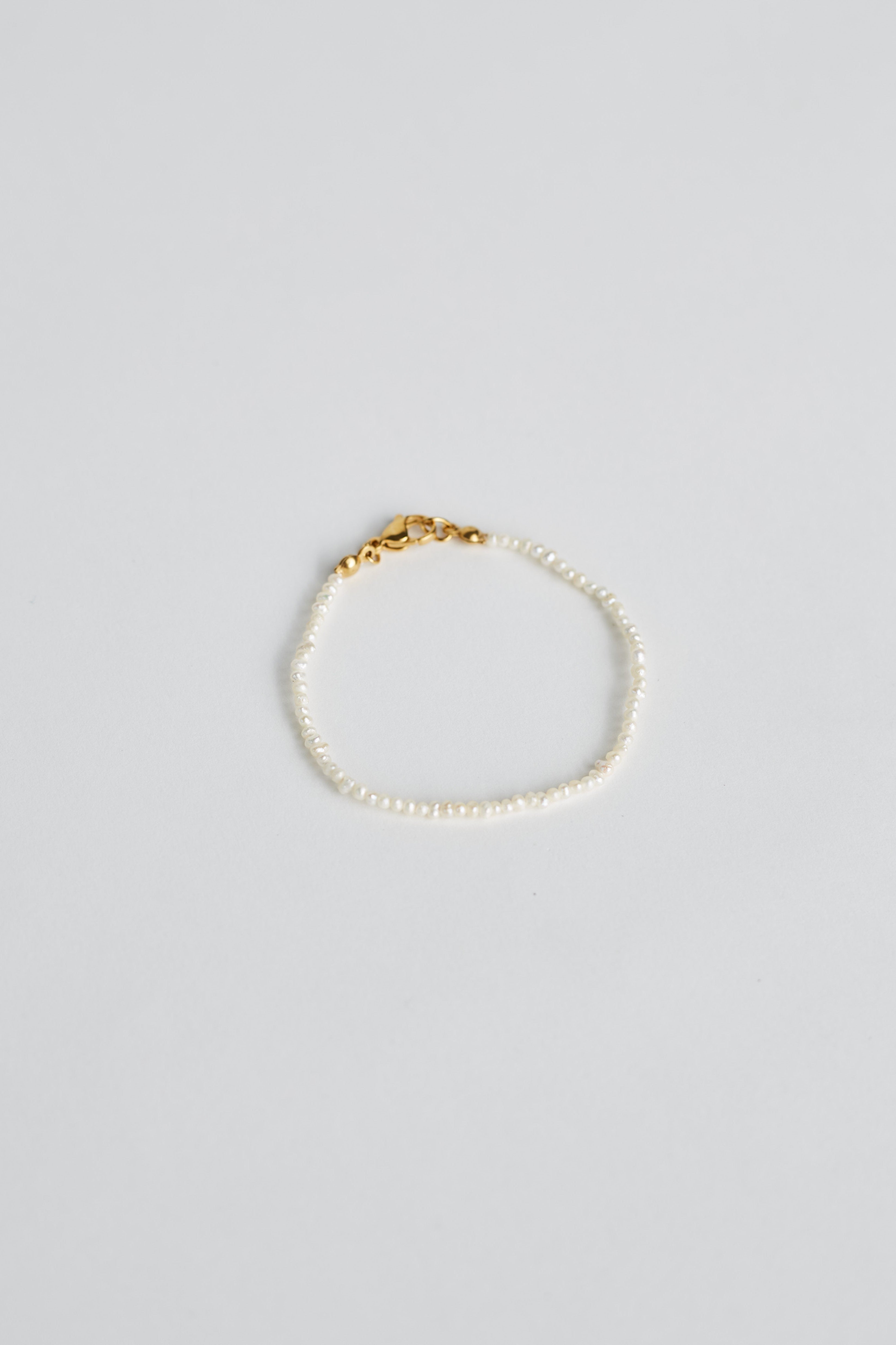 Tiny pearl bracelet with gold clasp on white background
