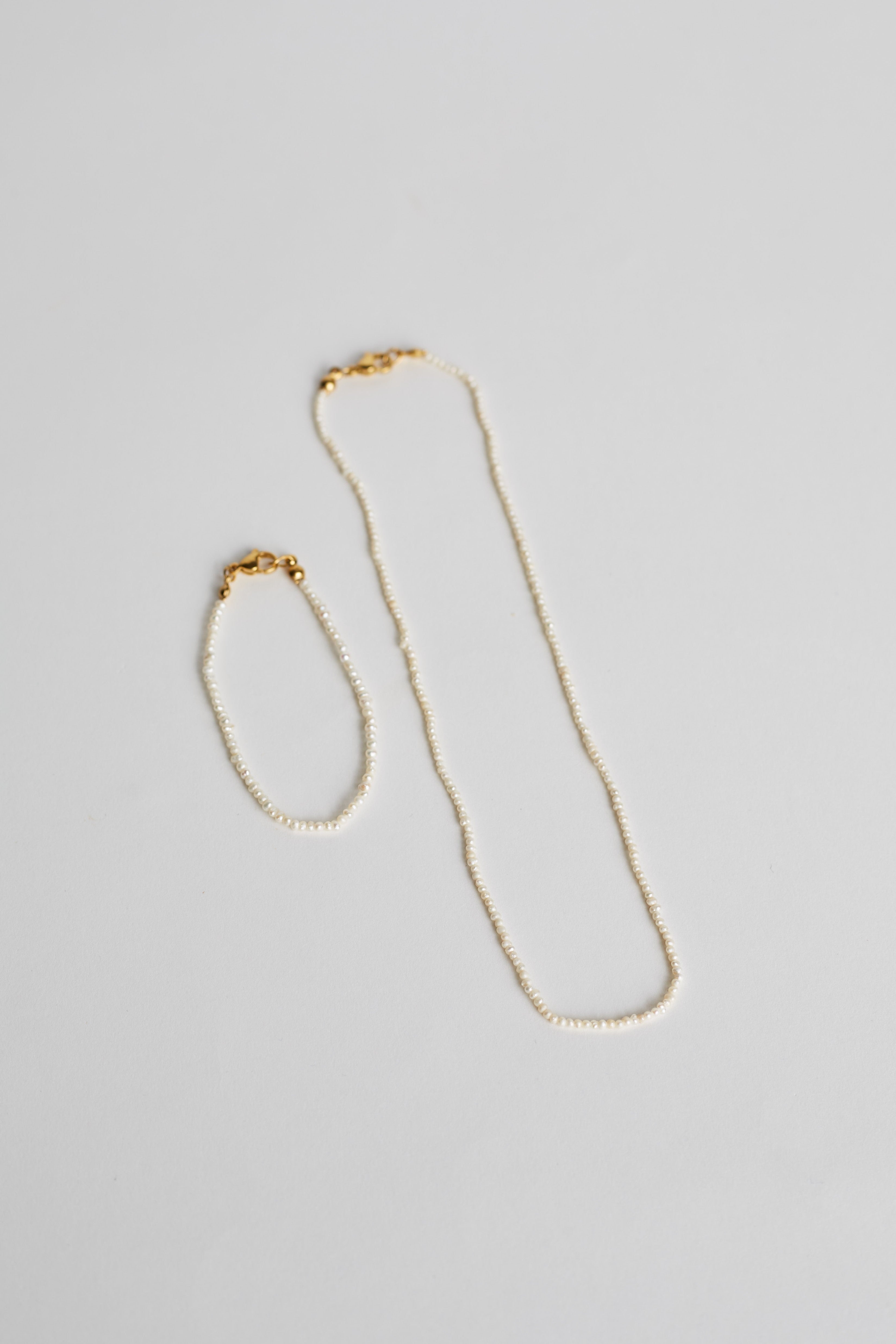 Gold necklace and bracelet set on a light gray background