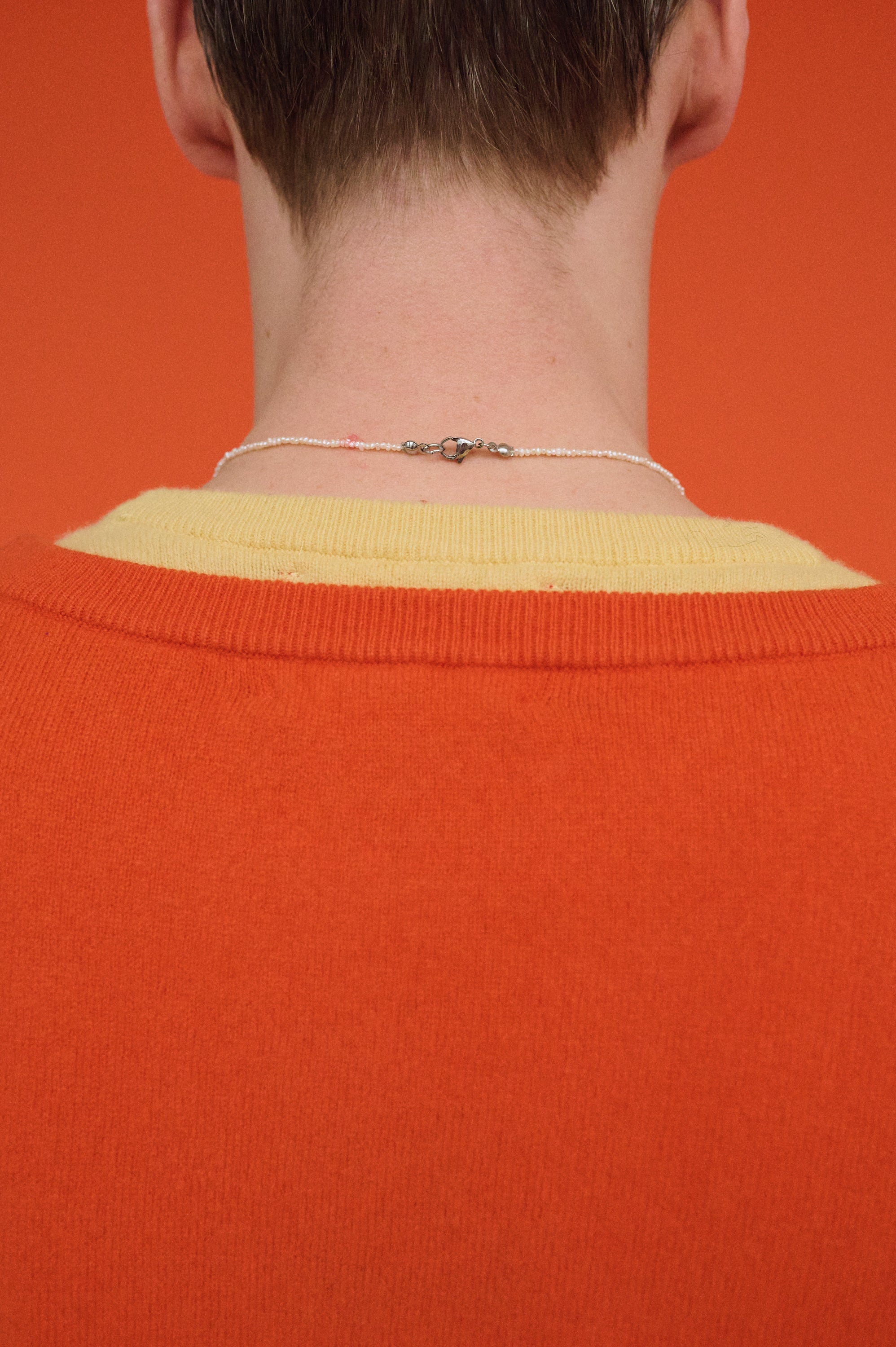 Back view of tiny white freshwater pearl necklace clasp on man’s neck.