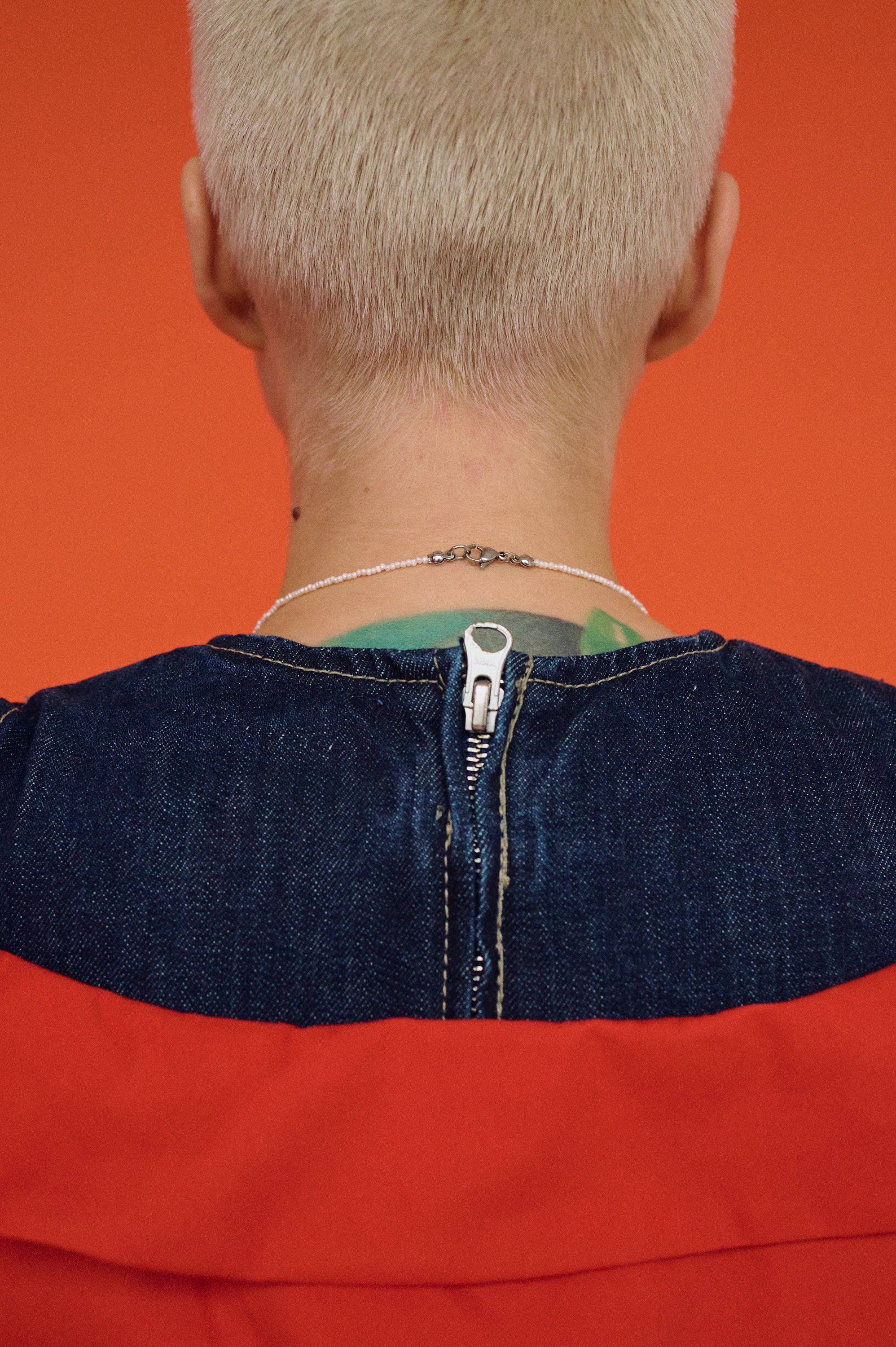 Person wearing a freshwater pearl necklace in silver clasp, red shirt with a blue collar against an orange background