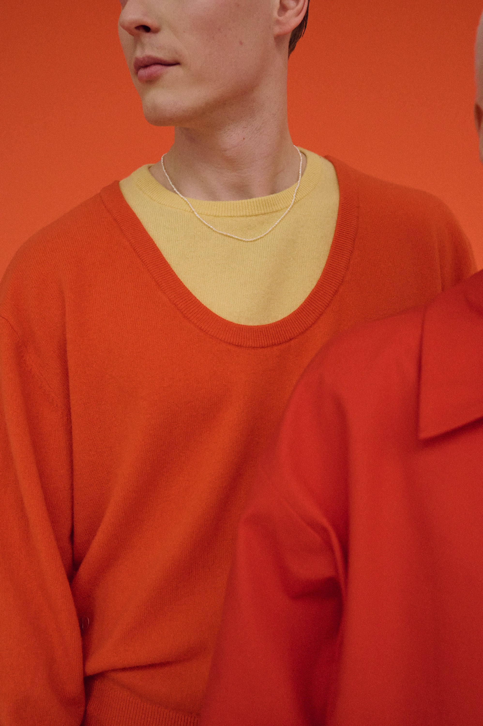 Close-up of man wearing tiny pearl necklace with yellow shirt and orange sweater.