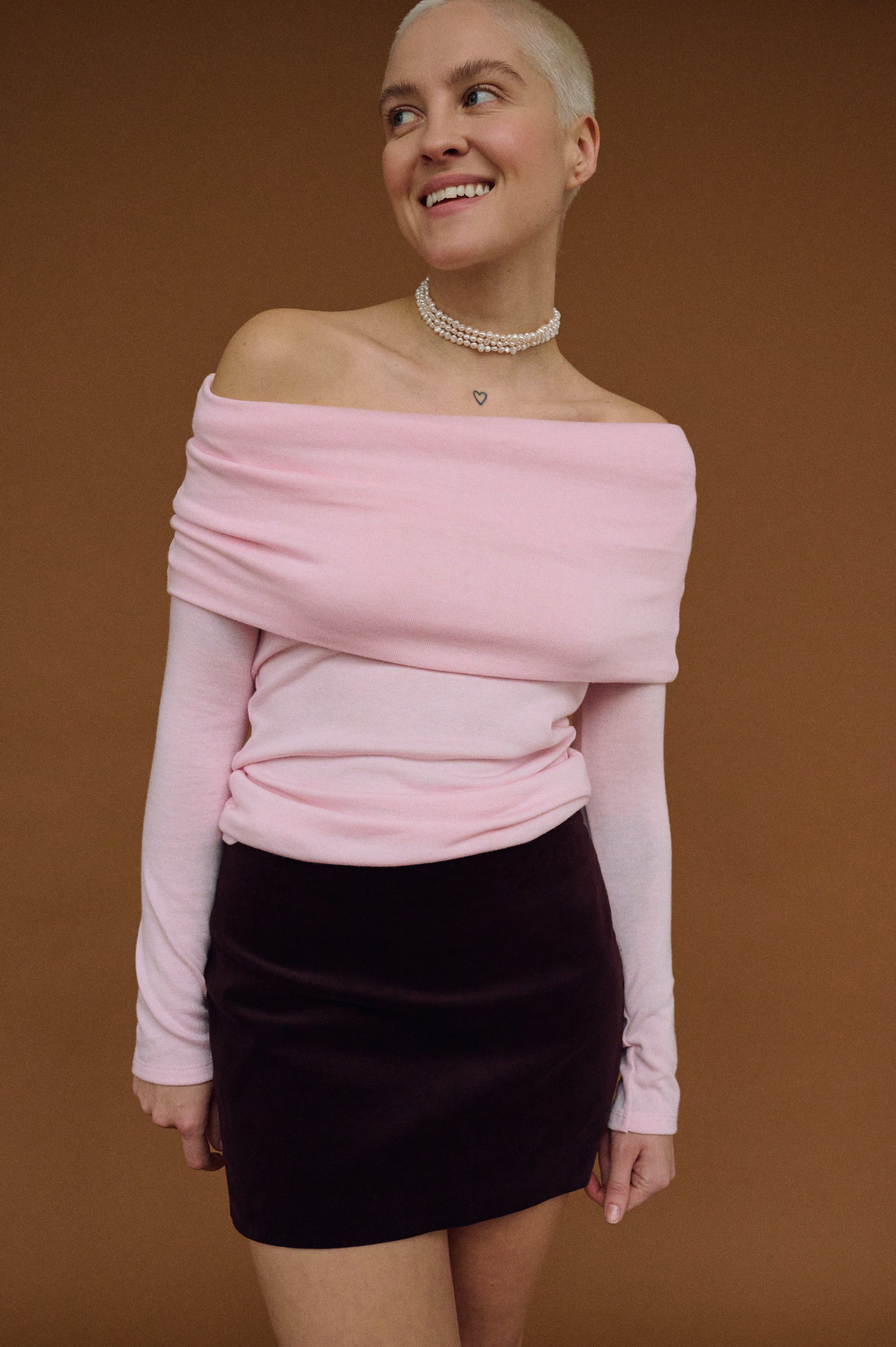 Smiling woman in pink off-shoulder top wearing layered pearl choker.