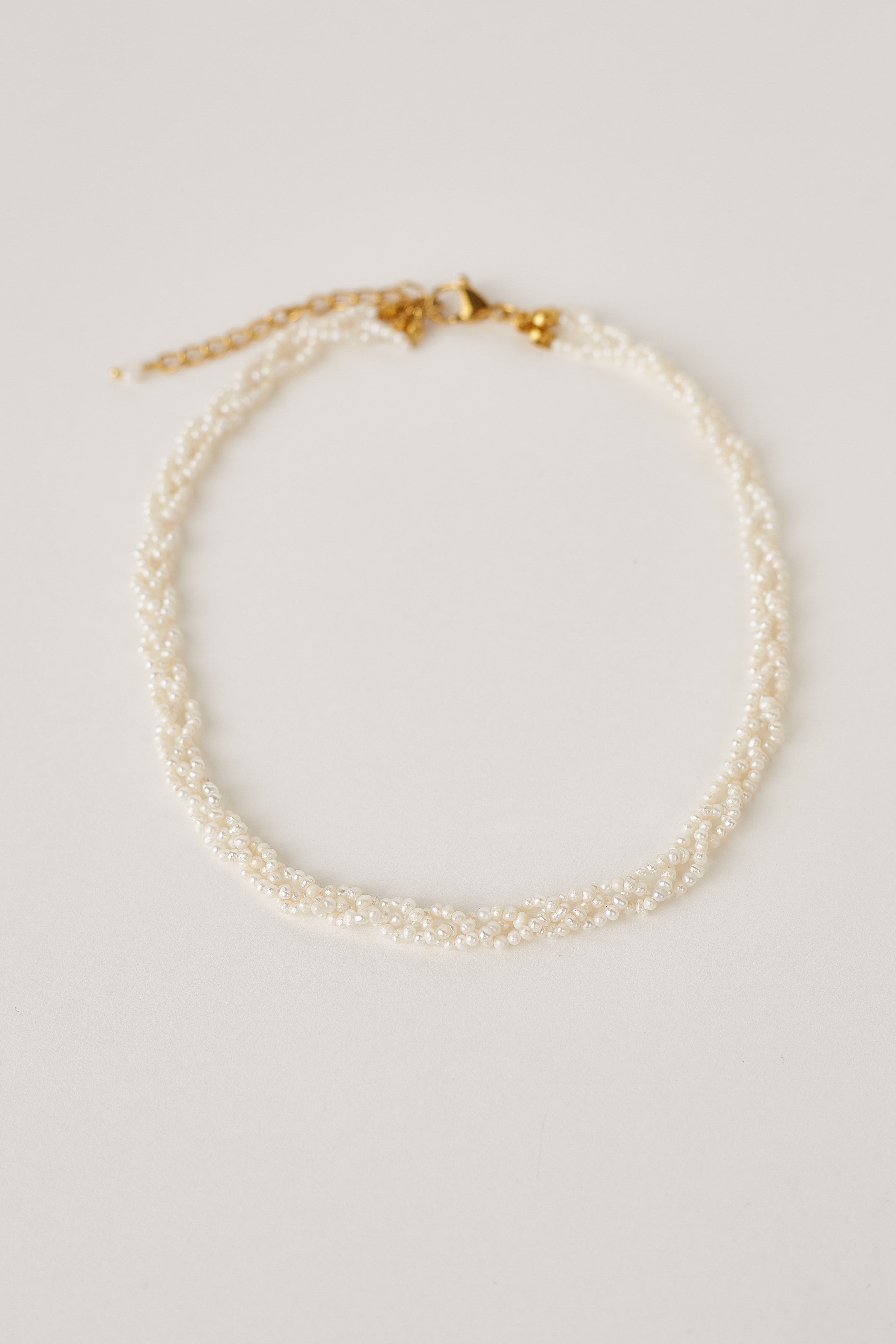Natural white pearl necklace on a light gray background with gold clasp