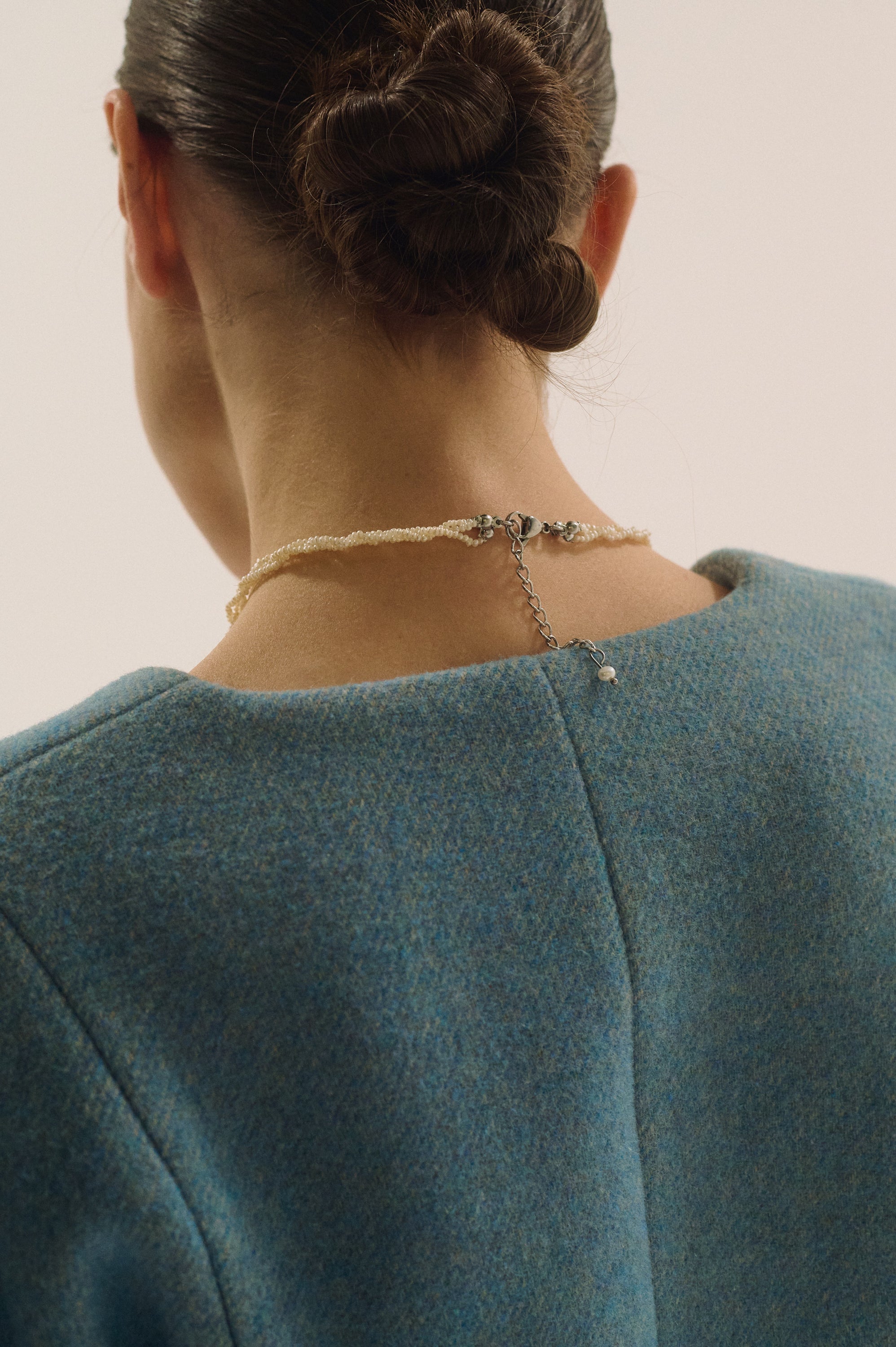 Close-up of the back of a woman’s neck wearing a triple strand tiny freshwater pearl necklace with silver clasp.