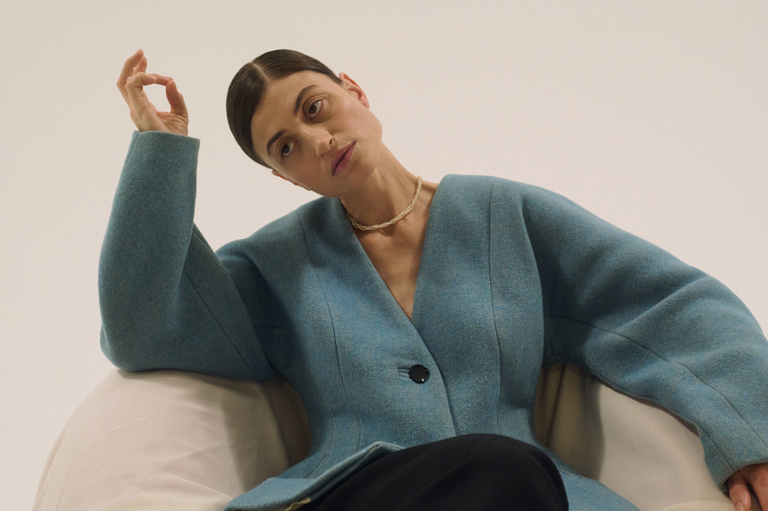 Woman in a blue structured jacket wearing a handcrafted triple strand pearl choker, looking to the side.