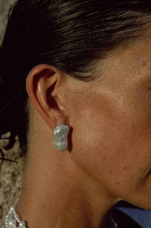 Close-up of handmade baroque pearl stud earrings on model outdoors
