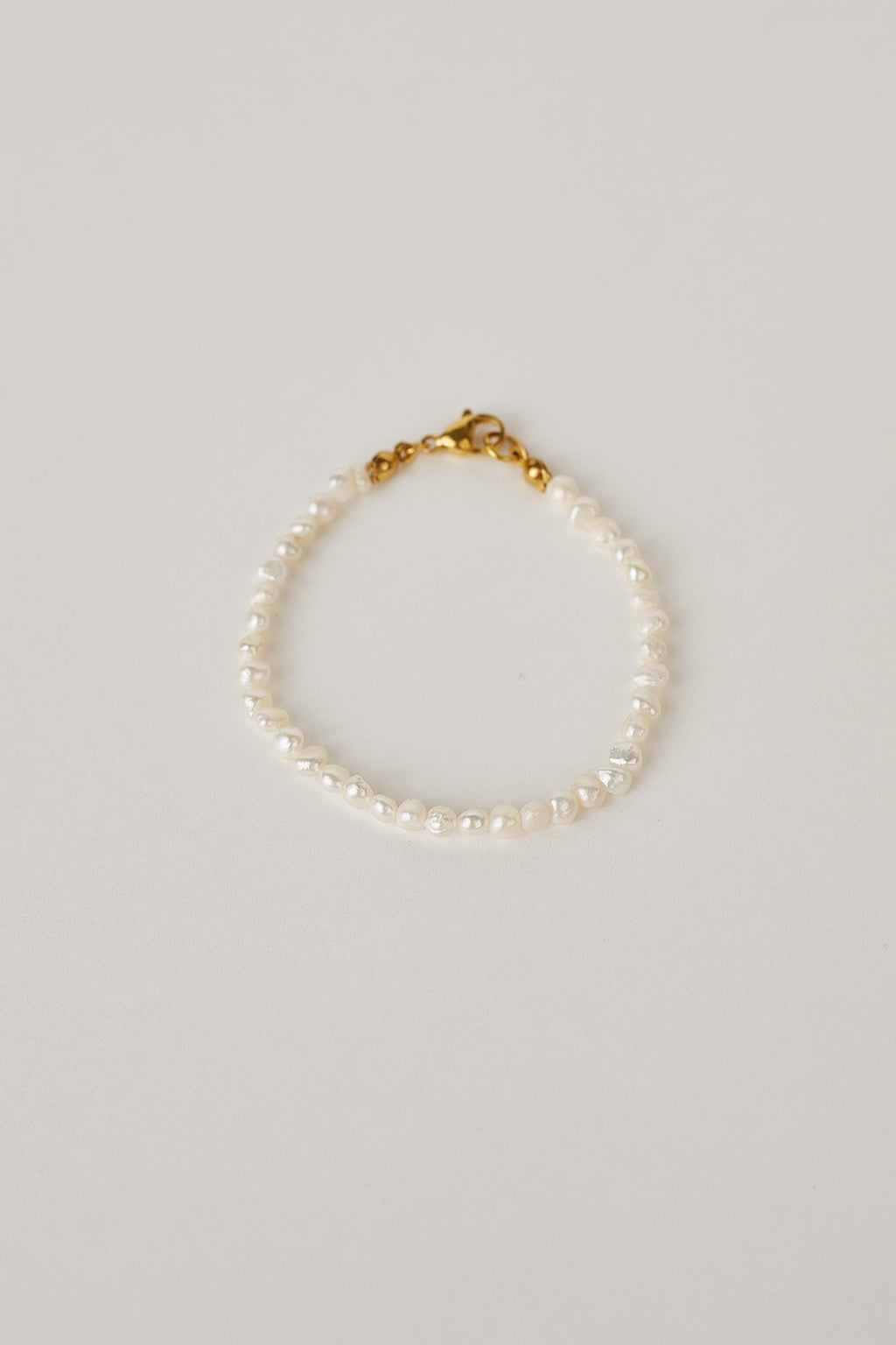 Pearl bracelet with a gold clasp on a light gray background