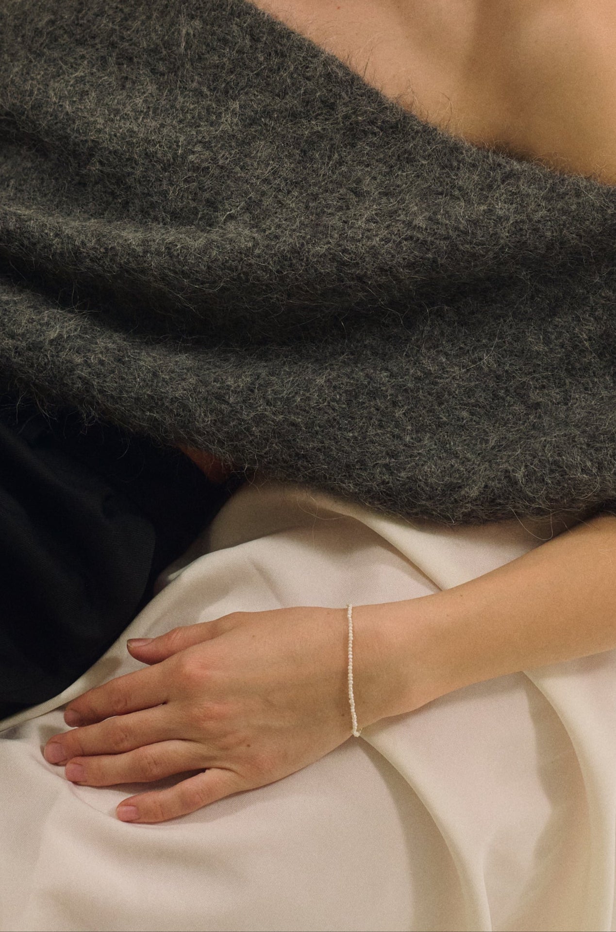 Woman wearing tiny pearl bracelet and minimal pearl necklace with grey off-shoulder sweater