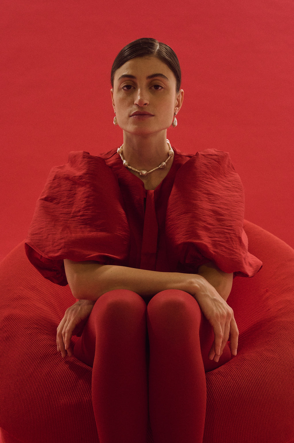 Woman wearing fitted necklace with baroque and stick pearls against red background
