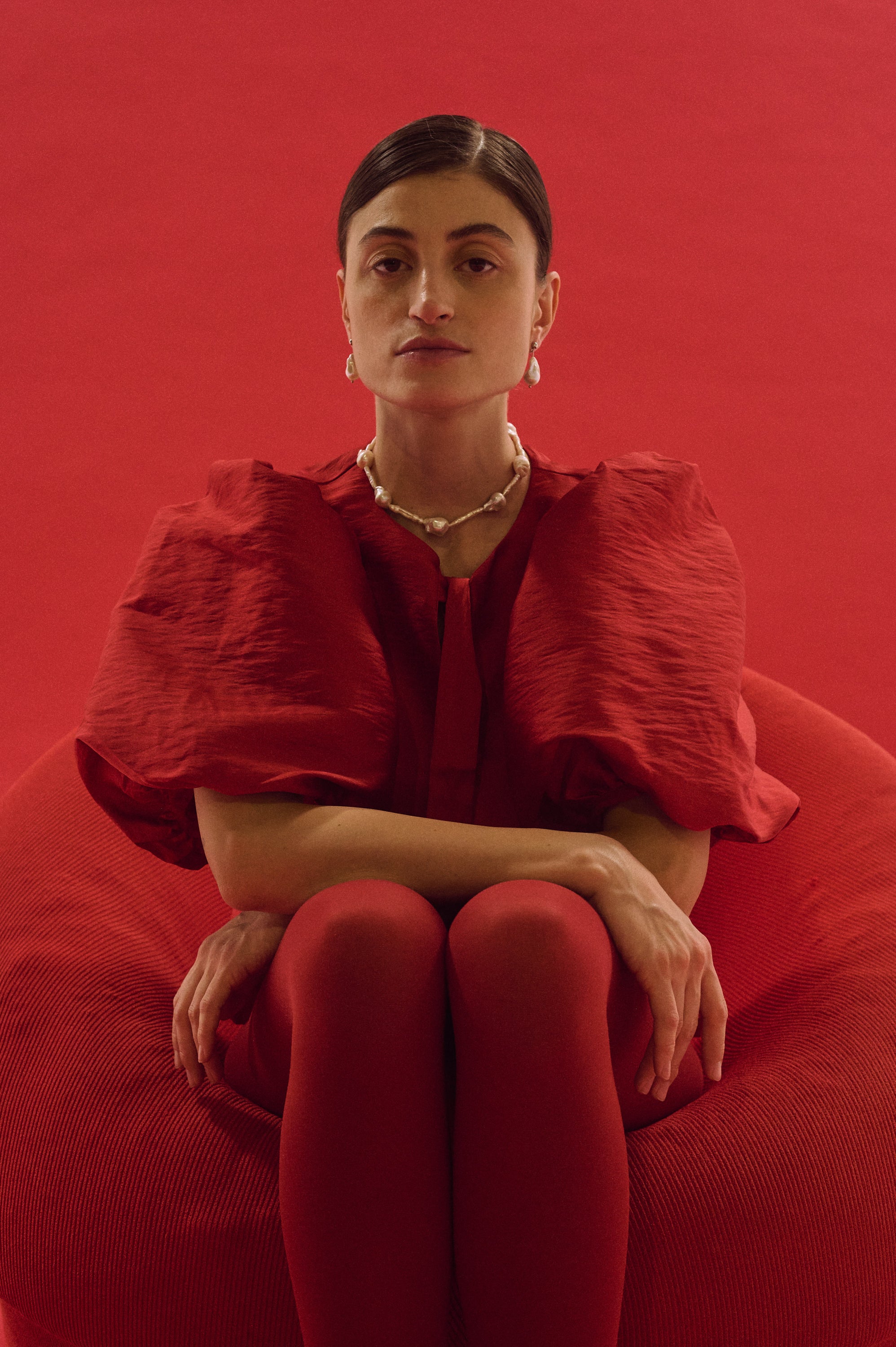 Woman wearing fitted necklace with baroque and stick pearls against red background