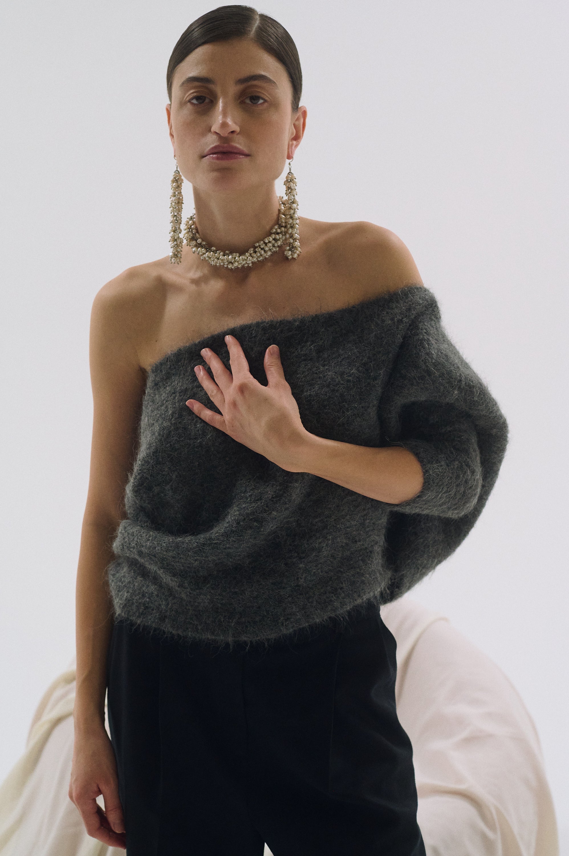 Woman wearing long bold statement pearl earrings with grey sweater