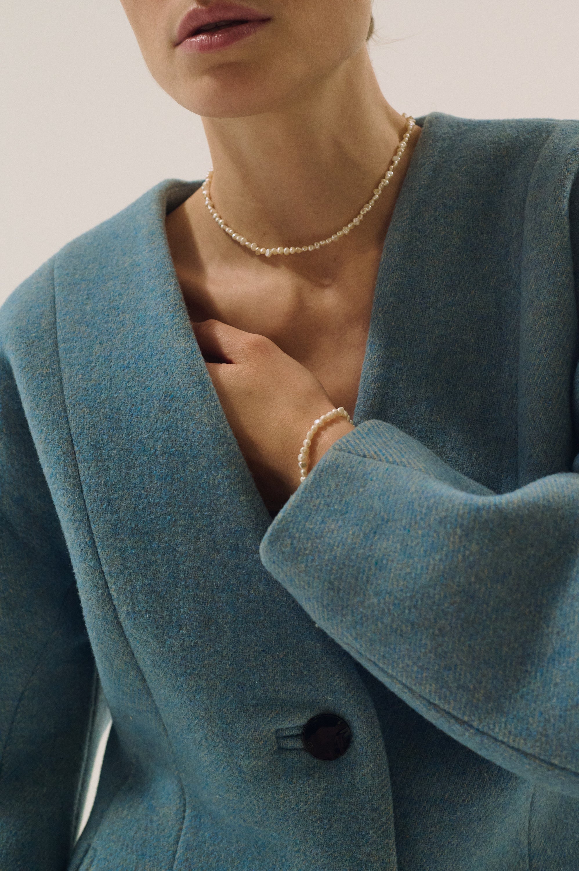 Close-up of hands showing a matching pearl bracelet and minimal pearl necklace.