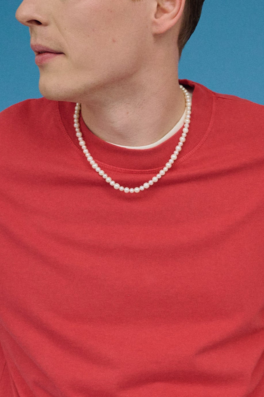Man wearing a real white freshwater pearl necklace styled with a red T-shirt.