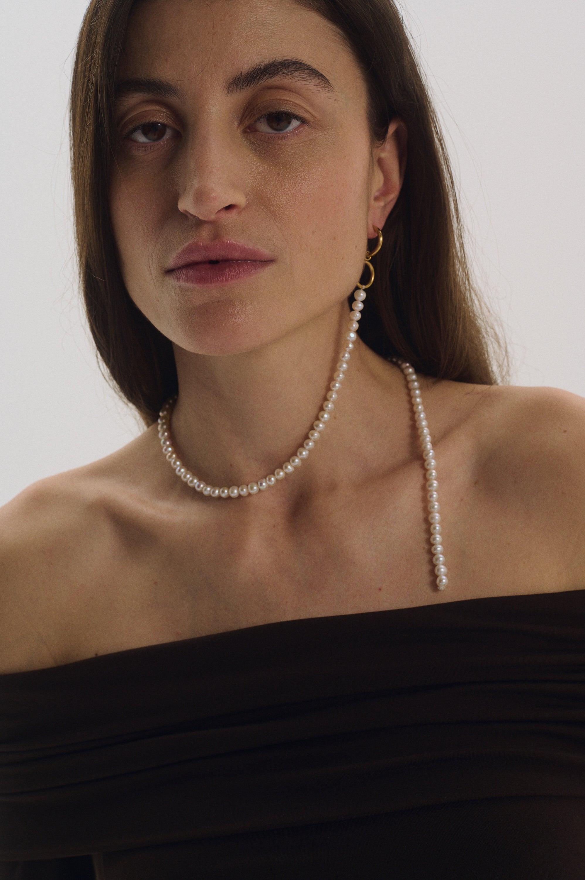 Single long dangling pearl earring styled with off-shoulder top