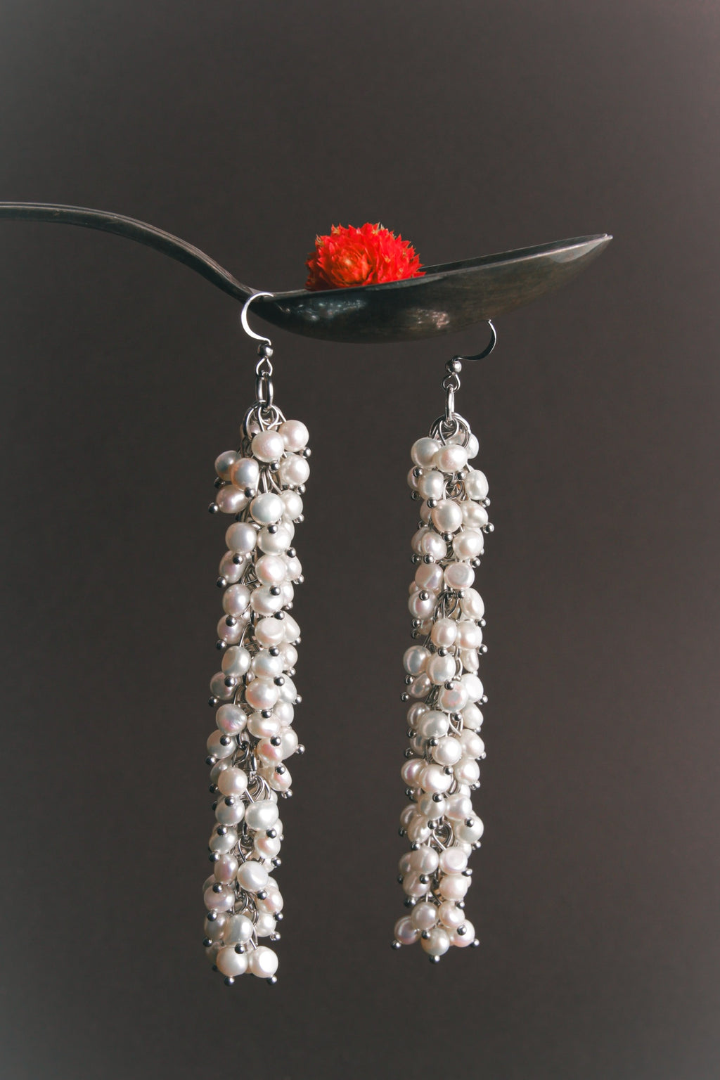 Pearl earrings hanging from a spoon with a dark background