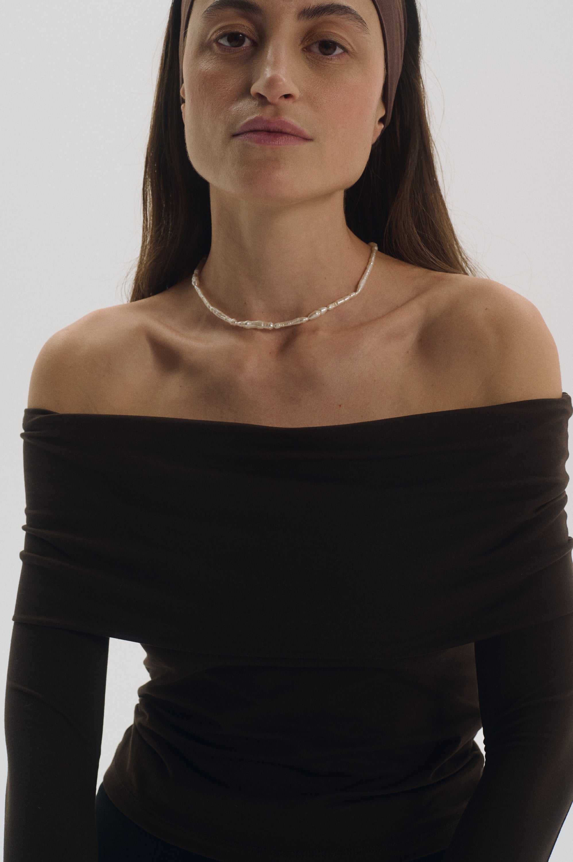 Model wearing natural stick pearl necklace with off-shoulder brown top.