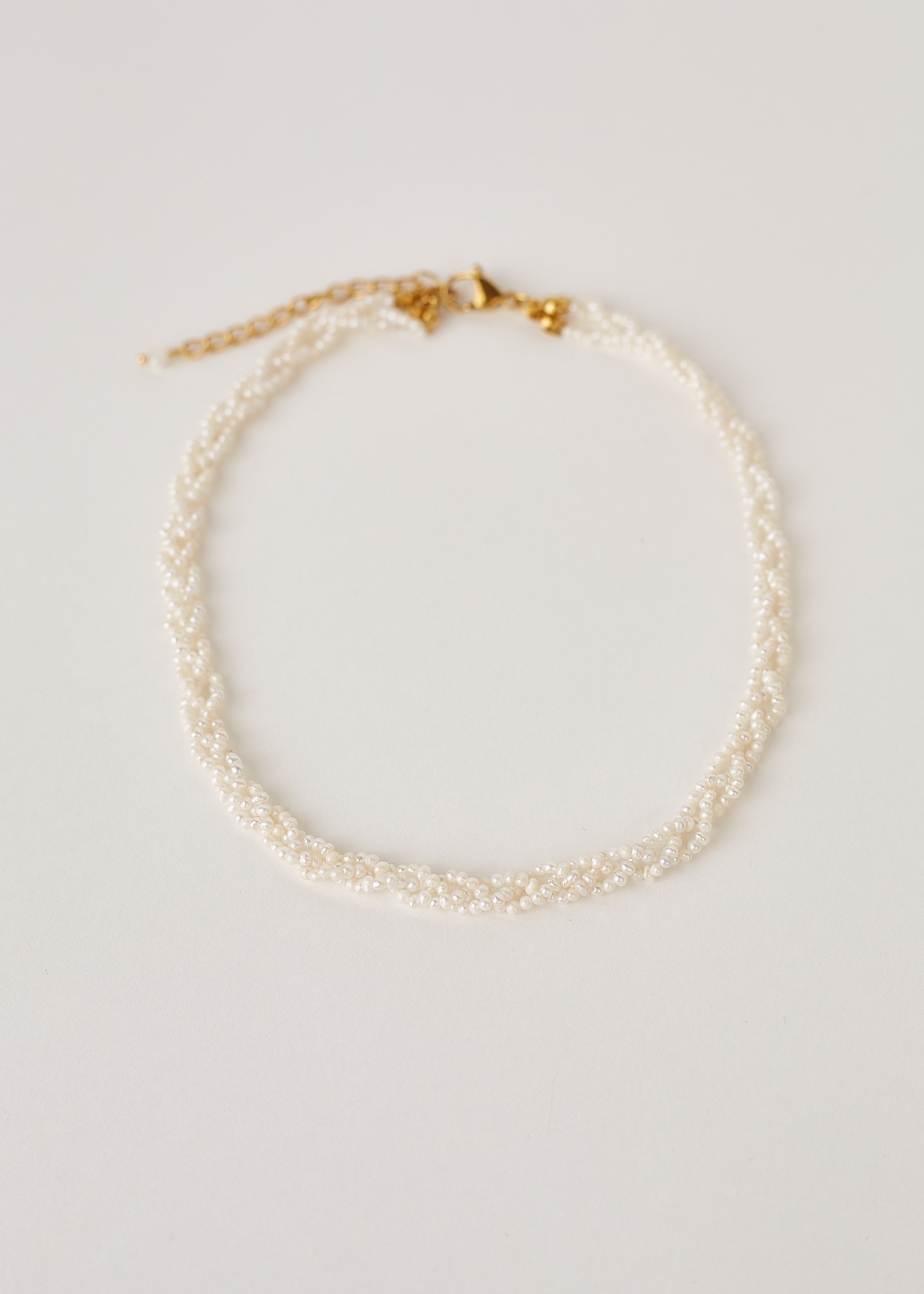 Natural white pearl necklace on a light gray background with gold clasp