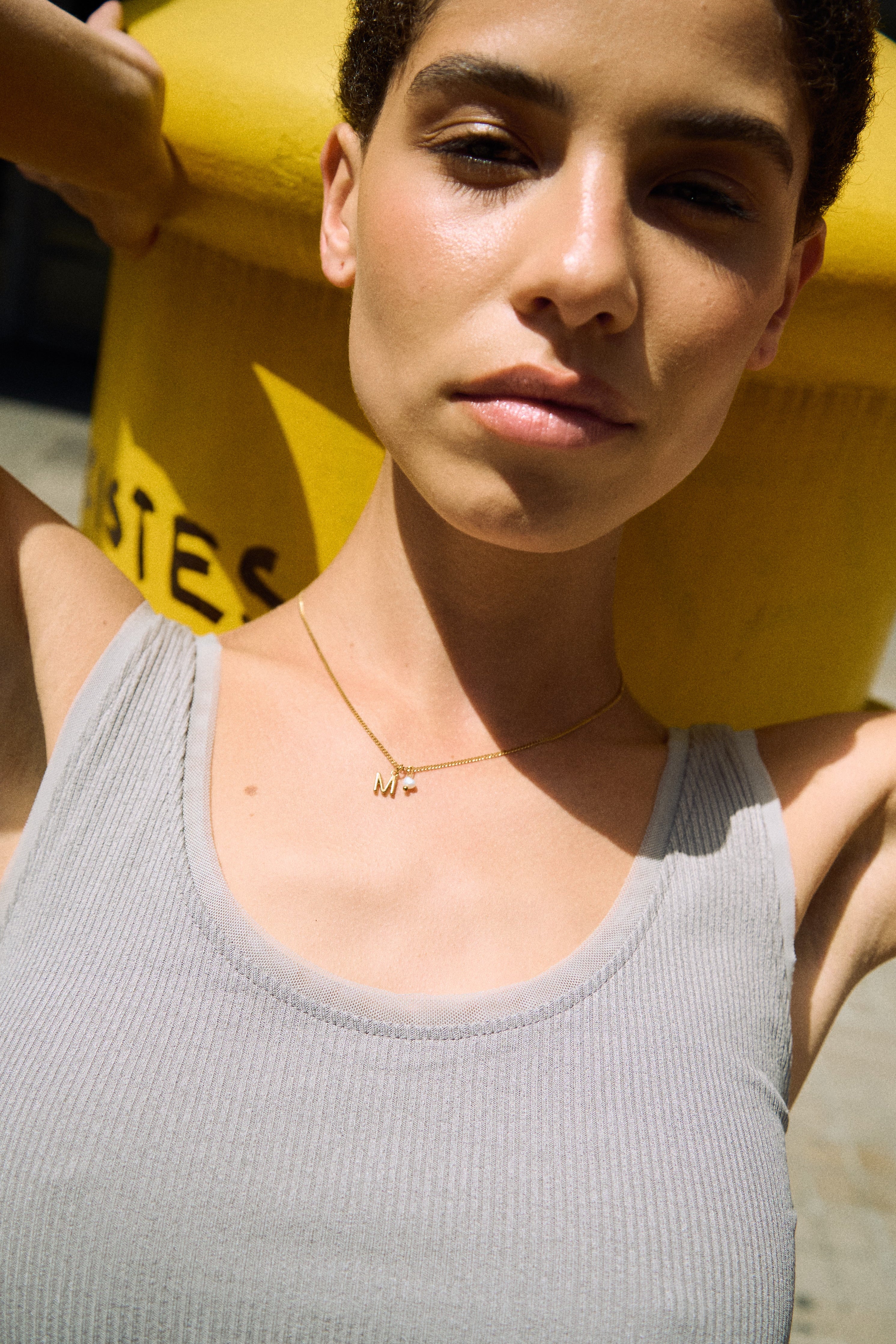 Model wearing a delicate initial necklace with a small letter pendant and tiny freshwater pearl.