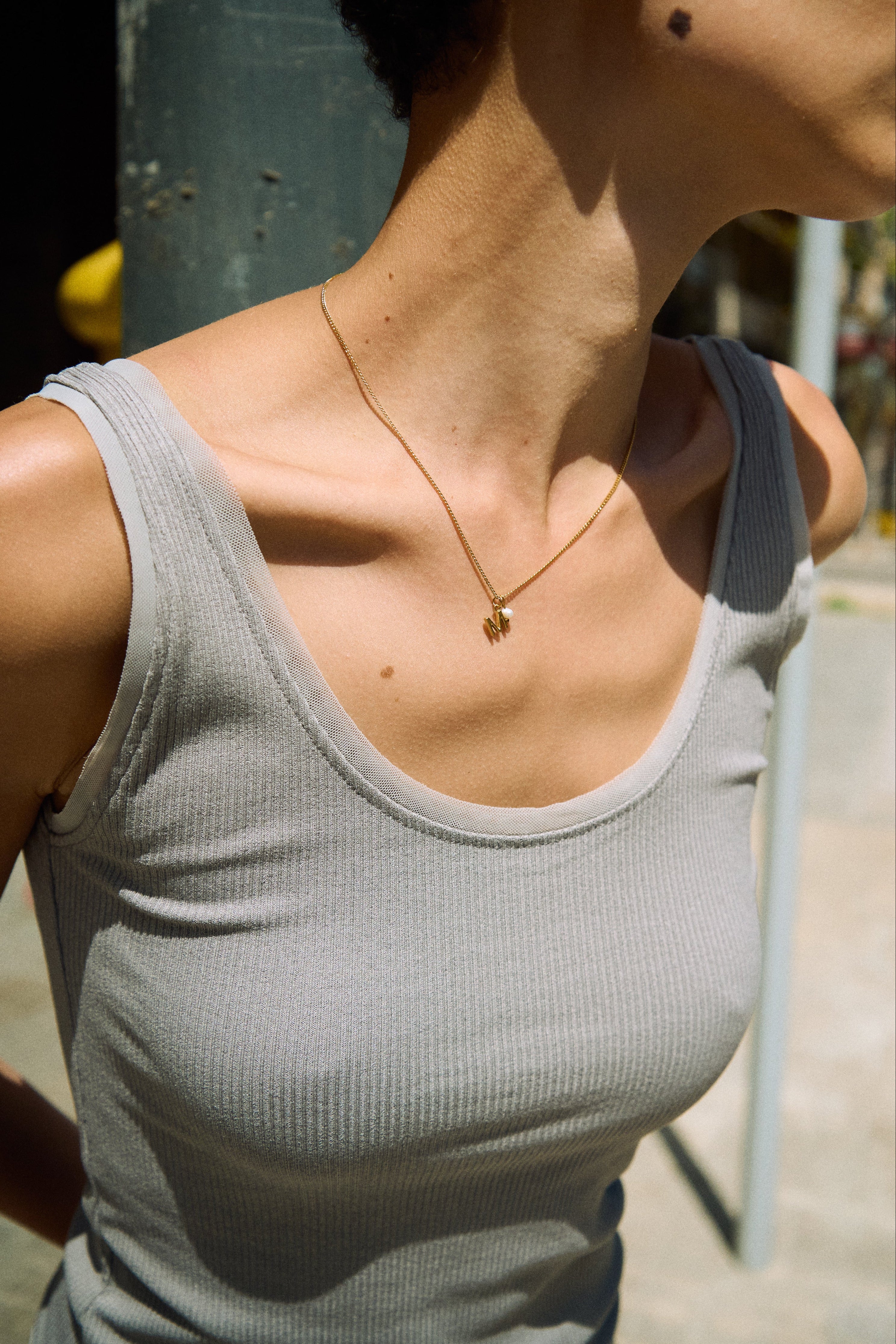 Model wearing a delicate initial necklace with a small letter pendant and tiny freshwater pearl.
