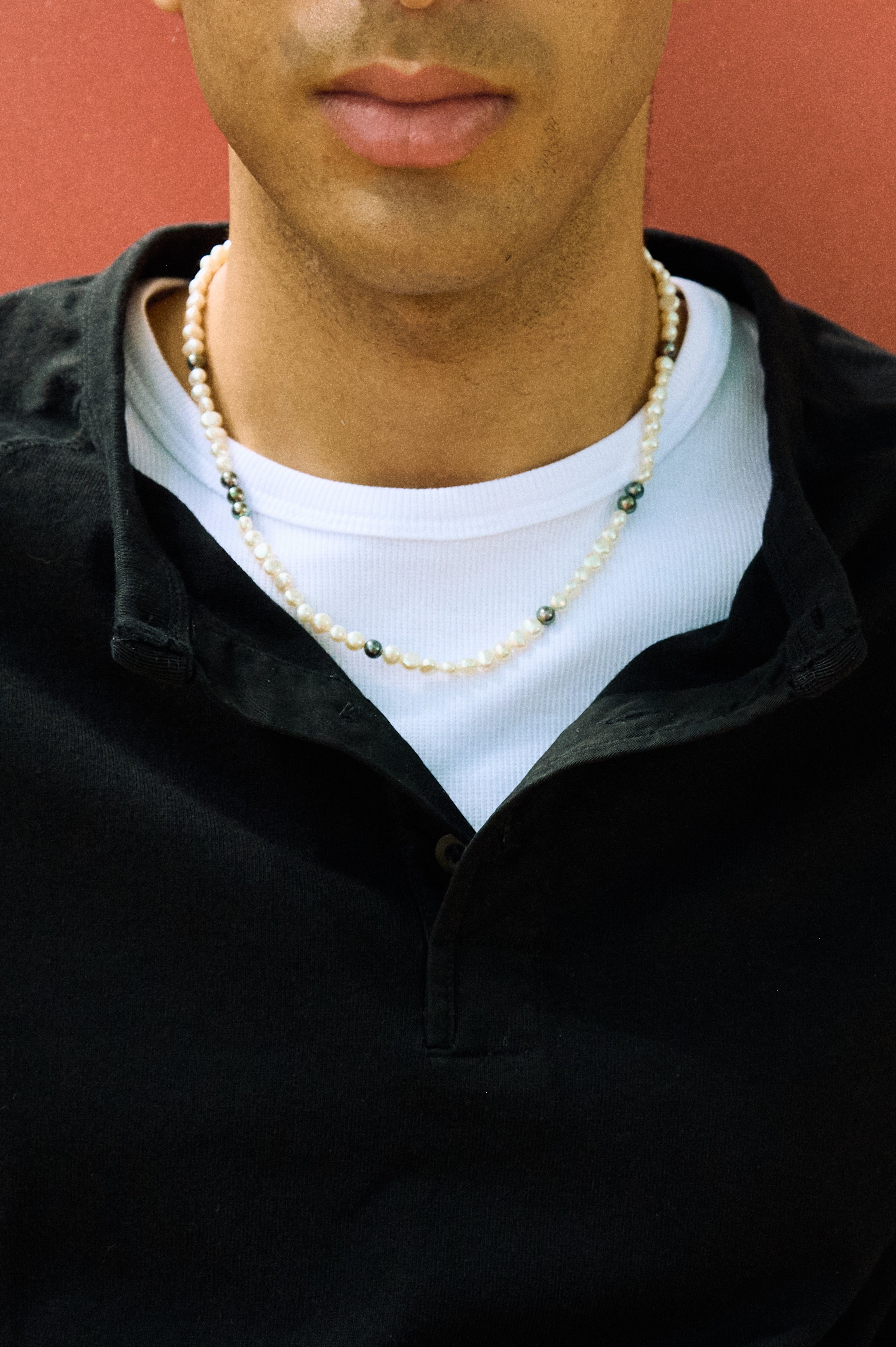 Close-up of a men’s pearl necklace with white nugget pearls and dark peacock pearl accents.