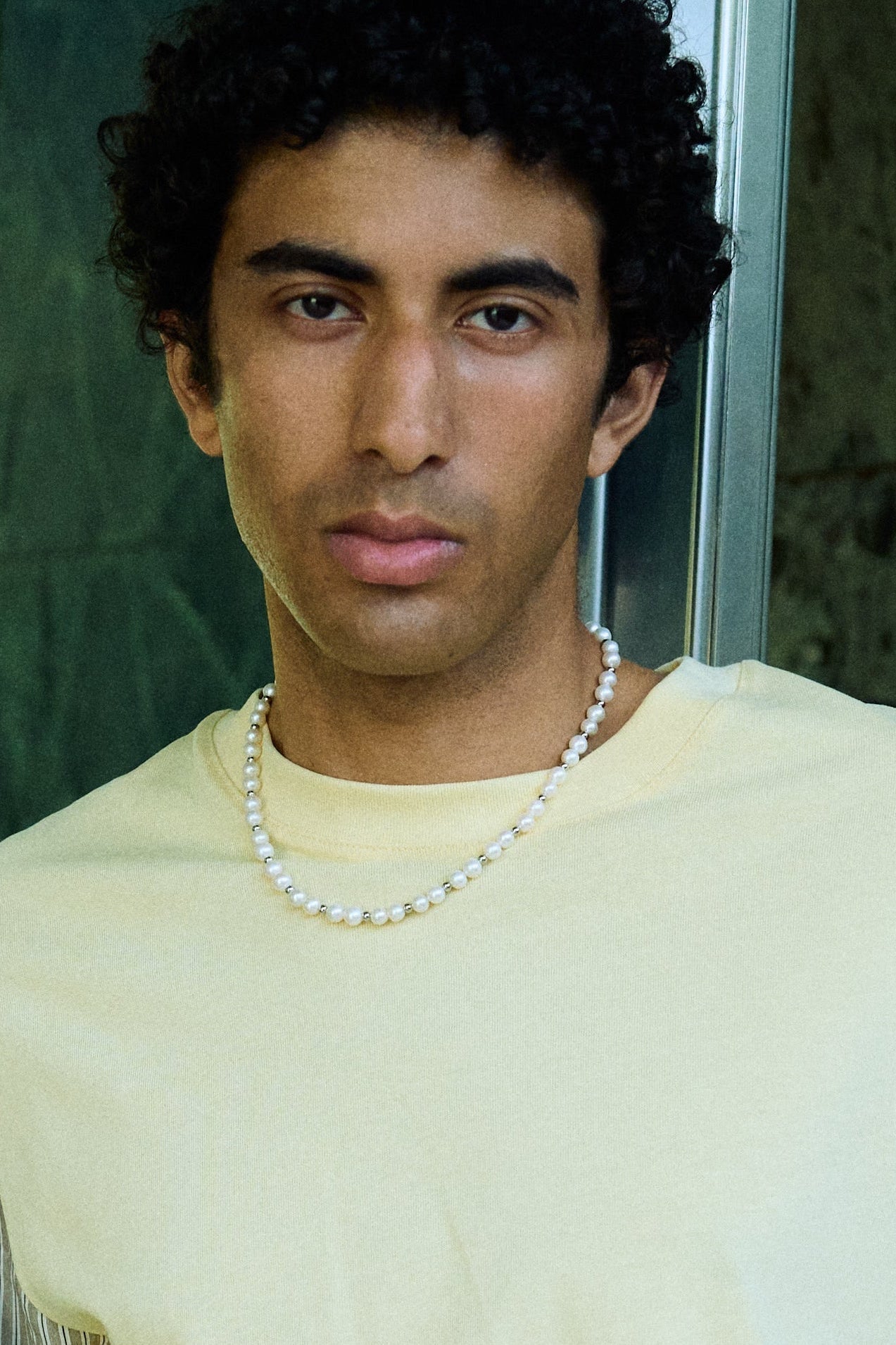 Man wearing a freshwater pearl necklace with round white pearls and metal bead accents.