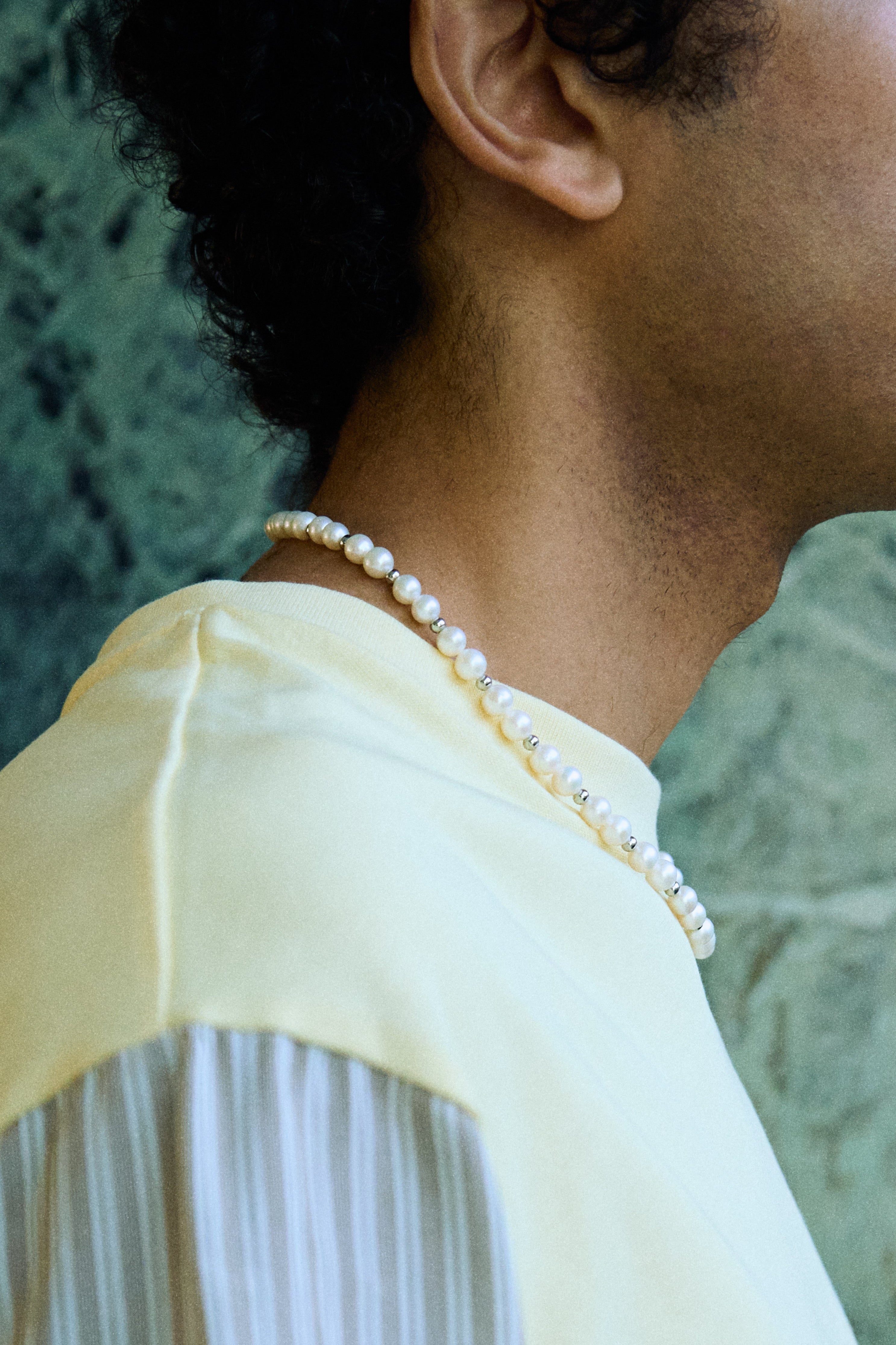 Man wearing a freshwater pearl necklace with round white pearls and metal bead accents.
