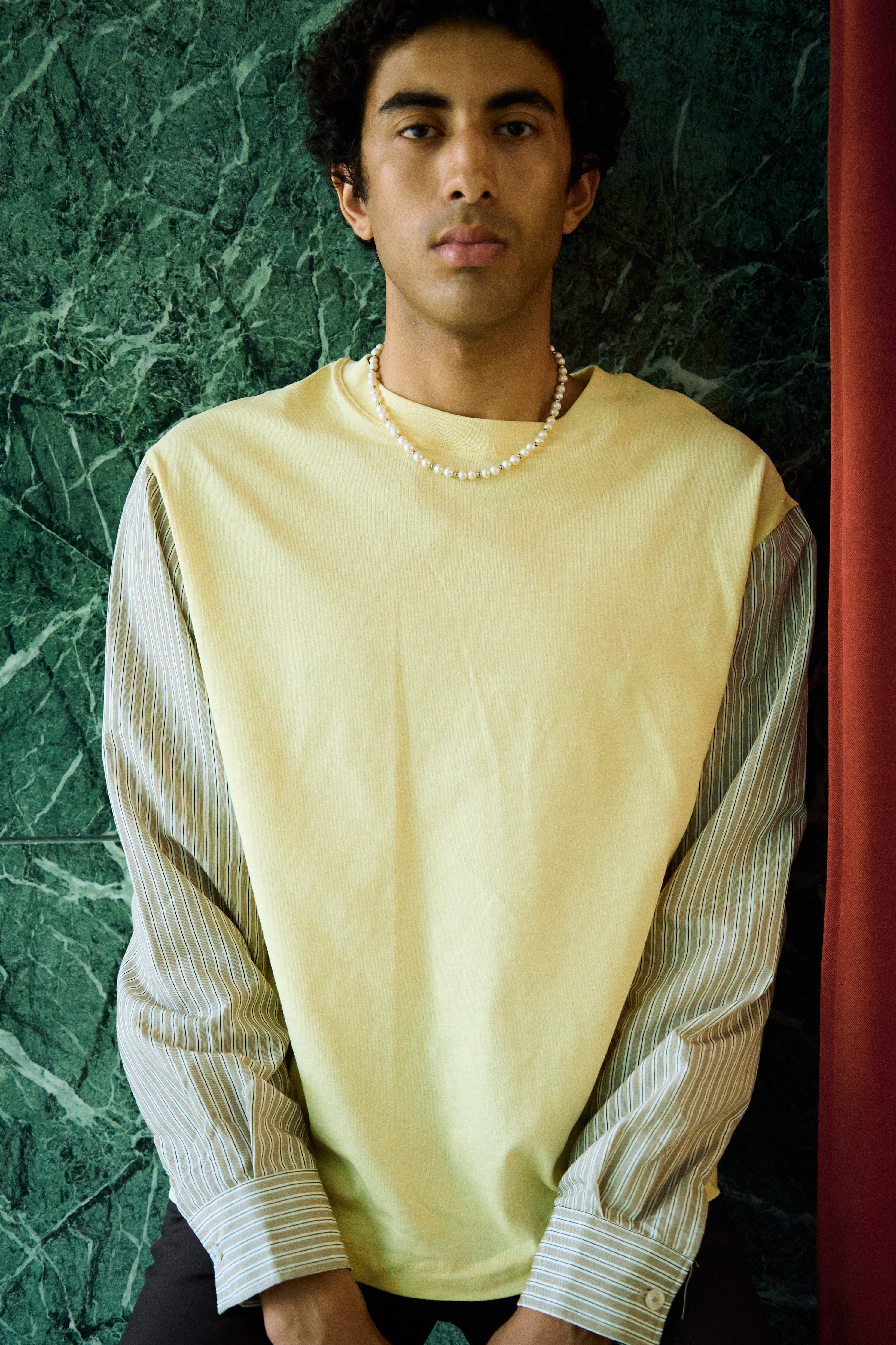 Man wearing a freshwater pearl necklace with round white pearls and metal bead accents.
