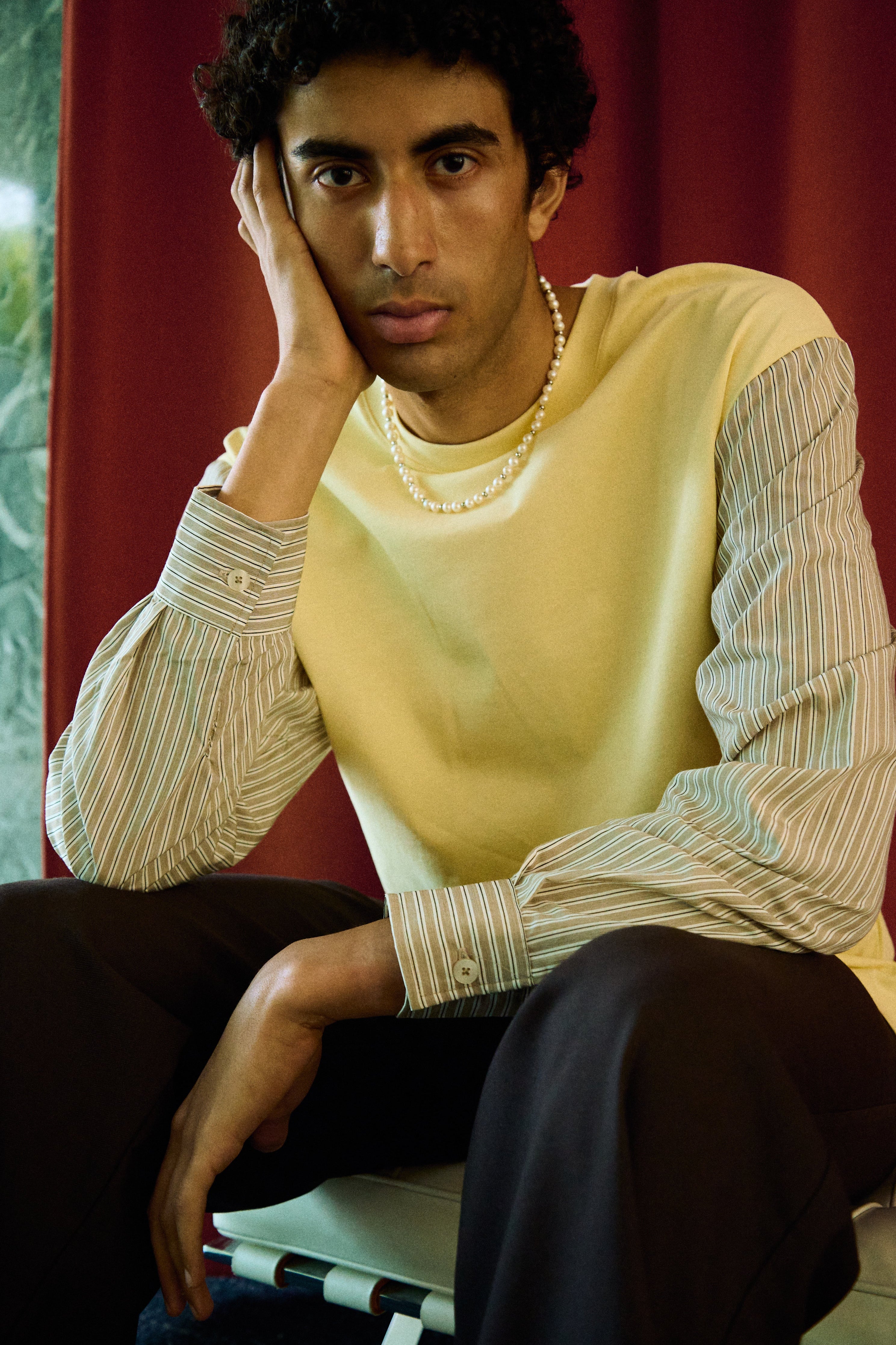 Man wearing a freshwater pearl necklace with round white pearls and metal bead accents.
