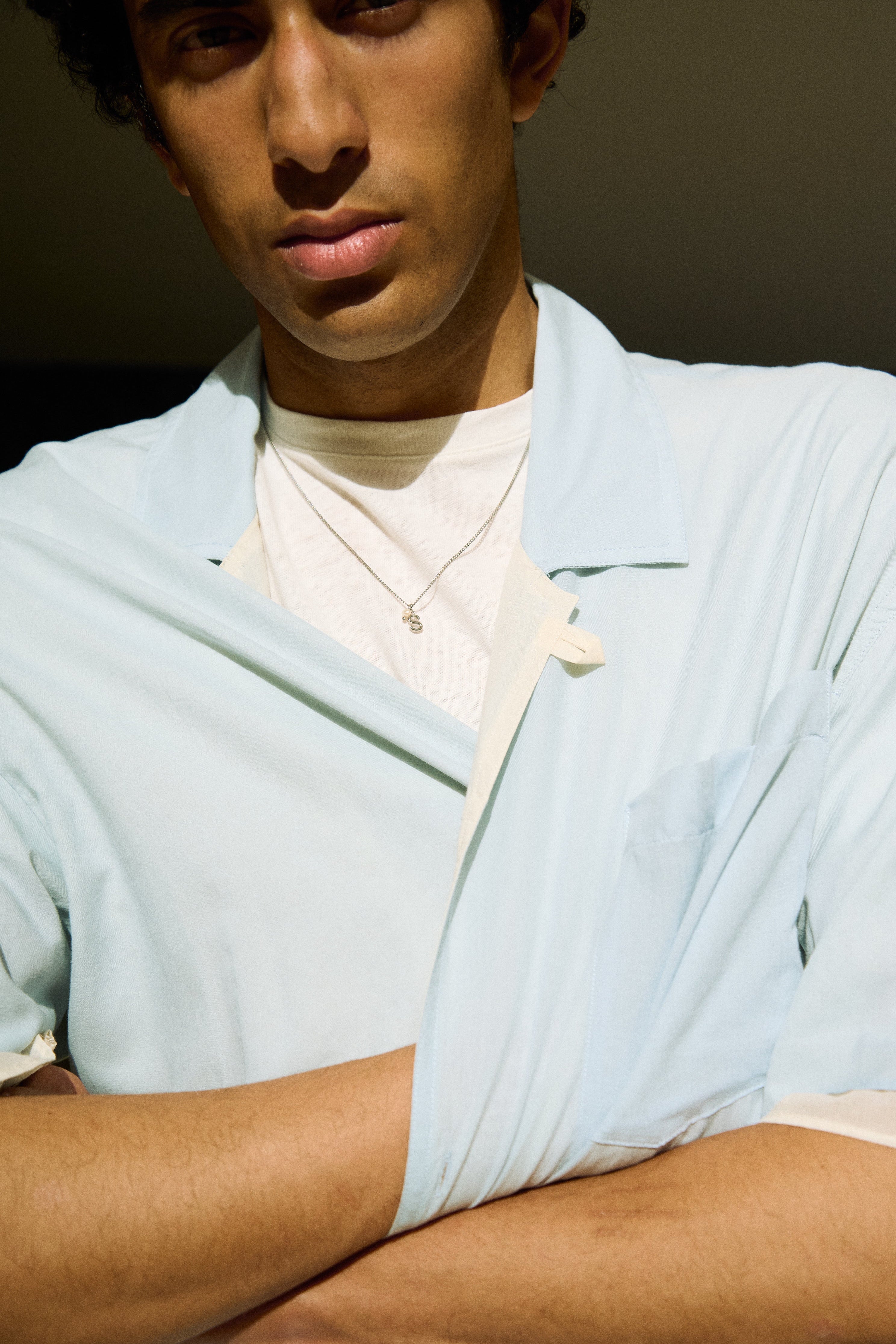Man wearing a minimal initial necklace with a small letter pendant on a longer chain.