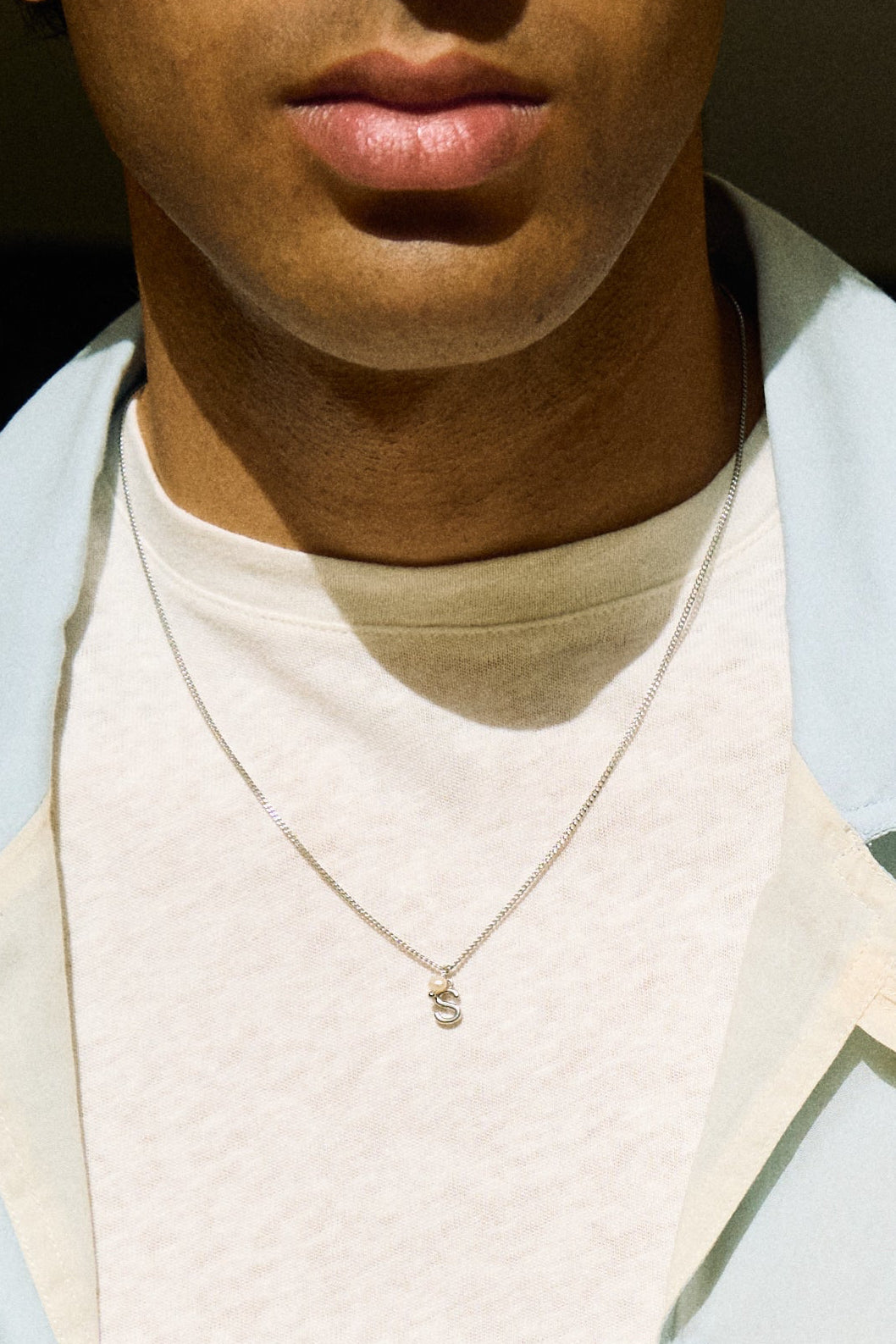 Man wearing a minimal initial necklace with a small letter pendant on a longer chain.