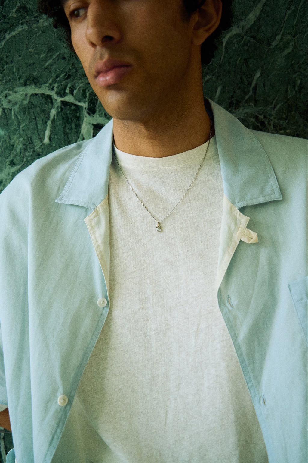 Man wearing a minimal initial necklace with a small letter pendant on a longer chain.