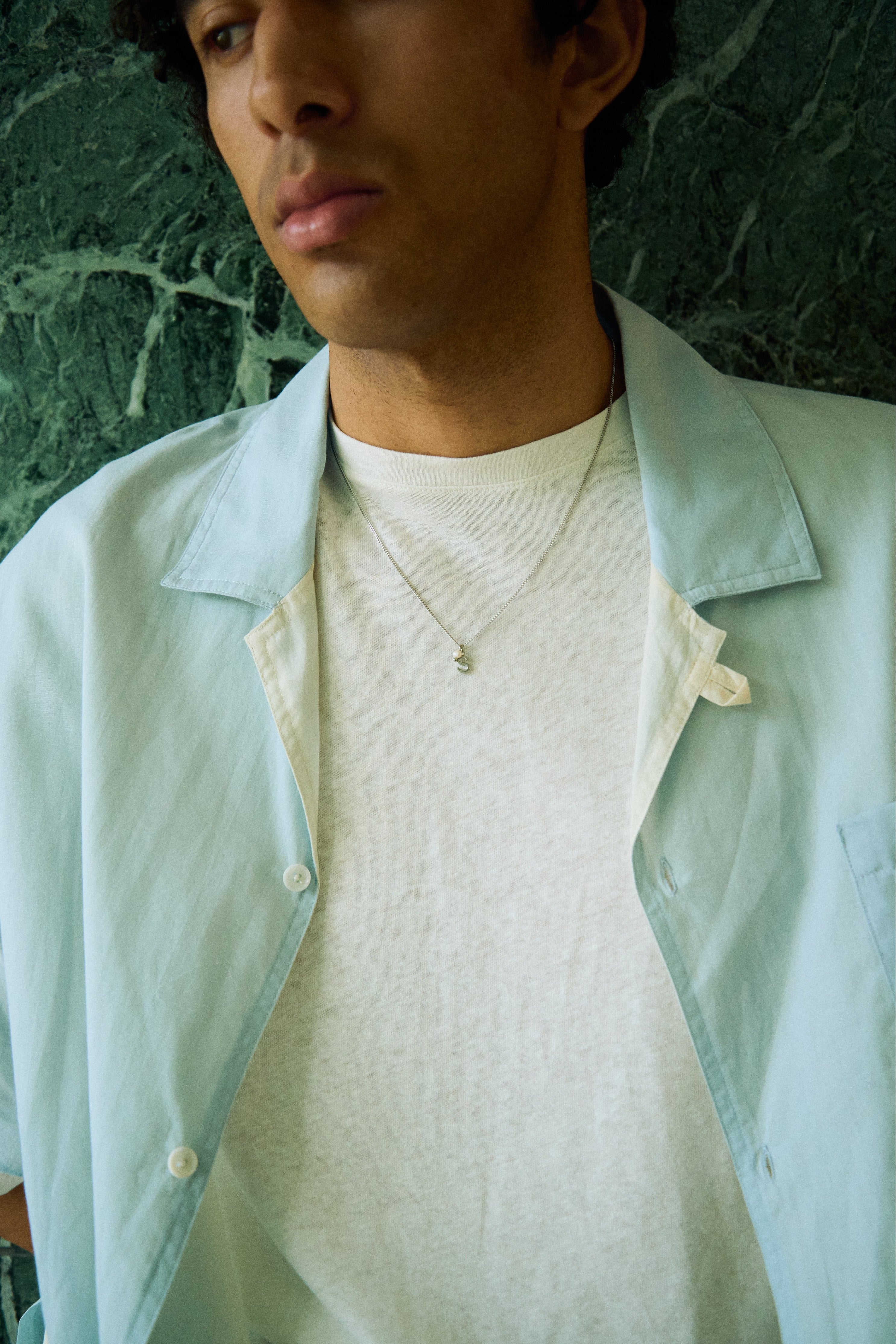 Man wearing a minimal initial necklace with a small letter pendant on a longer chain.
